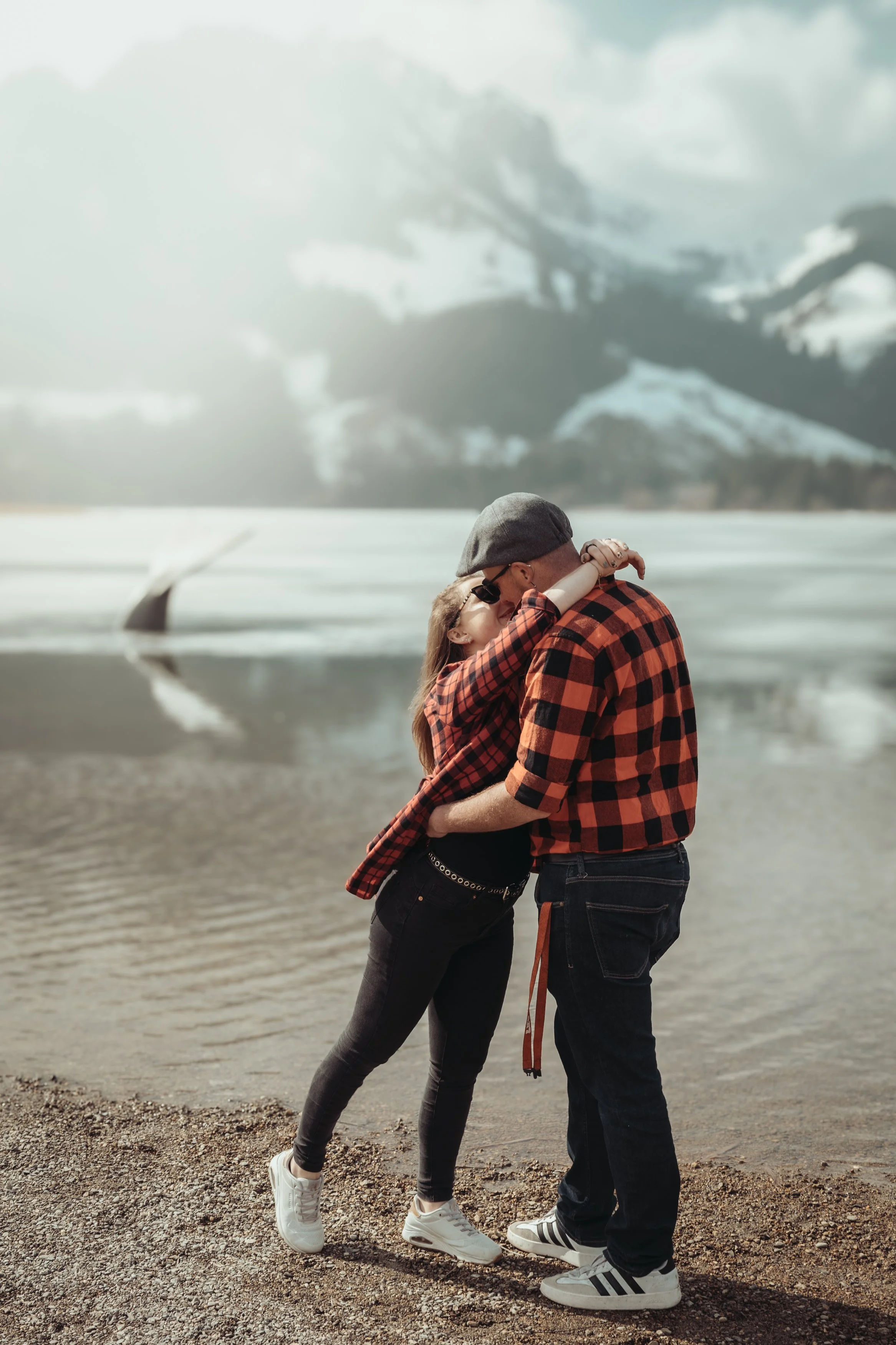 Un couple s'embrassant sur une plage en portant des vêtements à carreaux, avec un paysage de montagne en arrière-plan.