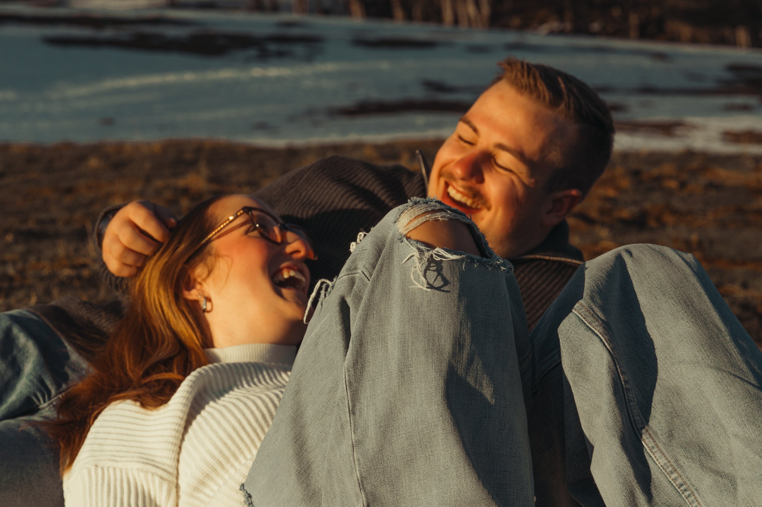Deux personnes rient et sourient sur une plage au coucher du soleil.