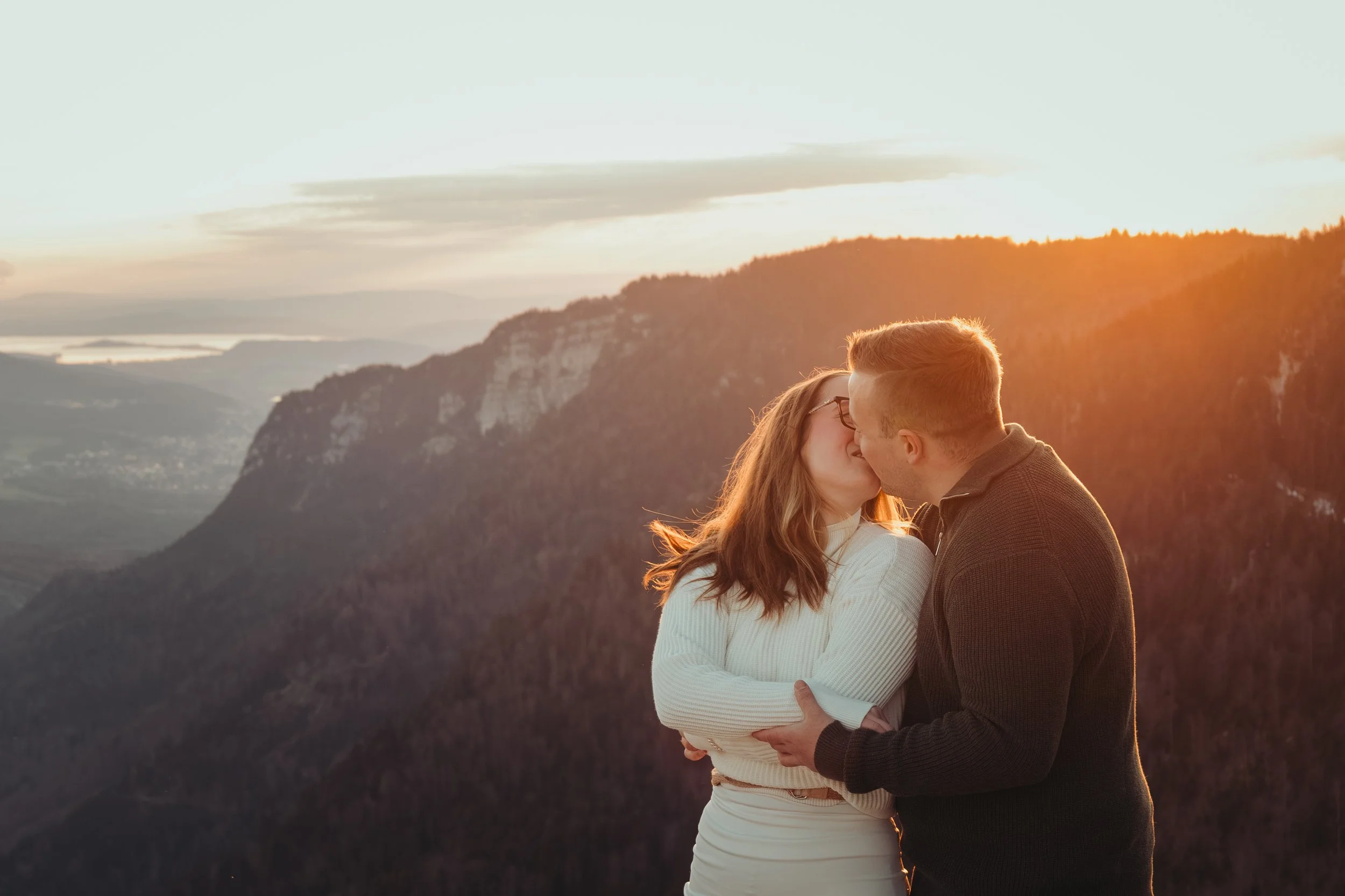 Un couple s'embrasse avec un paysage montagnard au coucher du soleil en arrière-plan.
