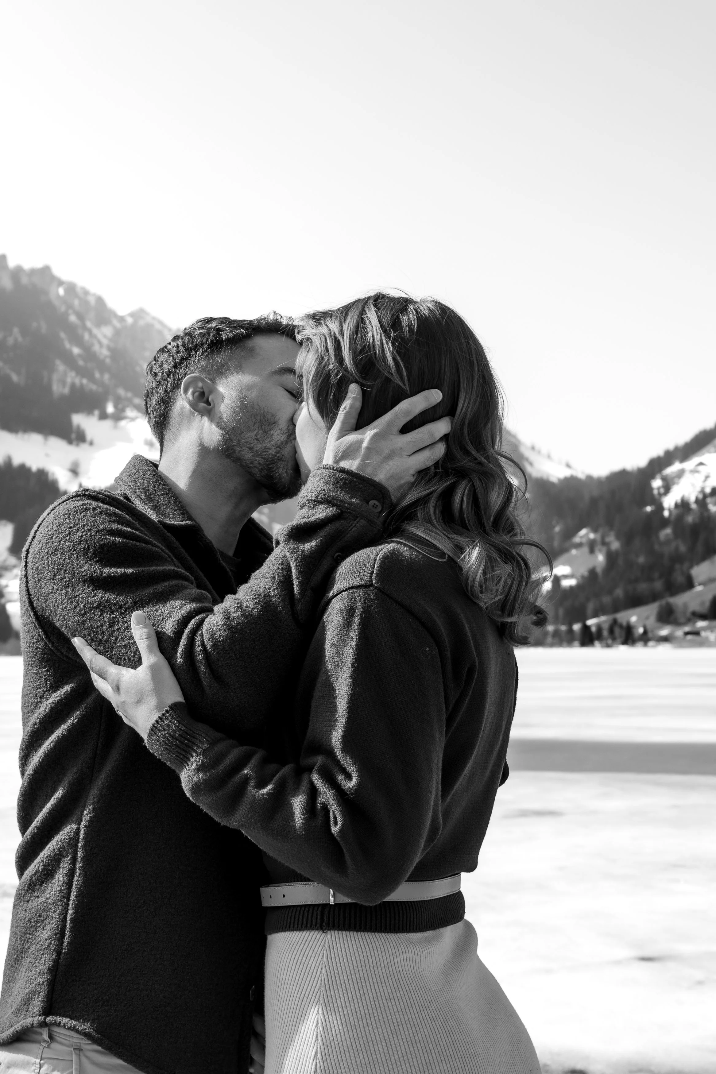 Un couple s'embrasse dans un paysage enneigé avec des montagnes en arrière-plan.