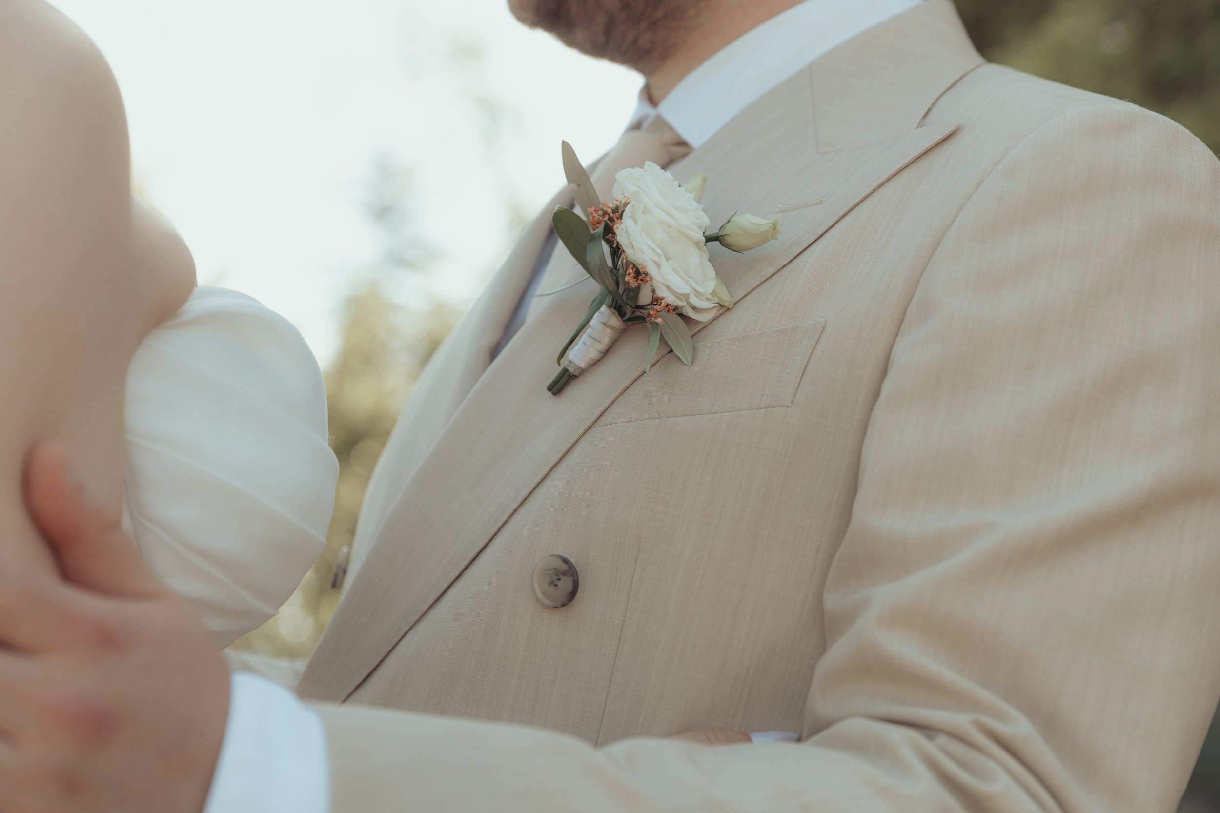 Groom en costume clair avec boutonnière de fleurs blanches et vertes lors d'un mariage, en pleine cérémonie.
