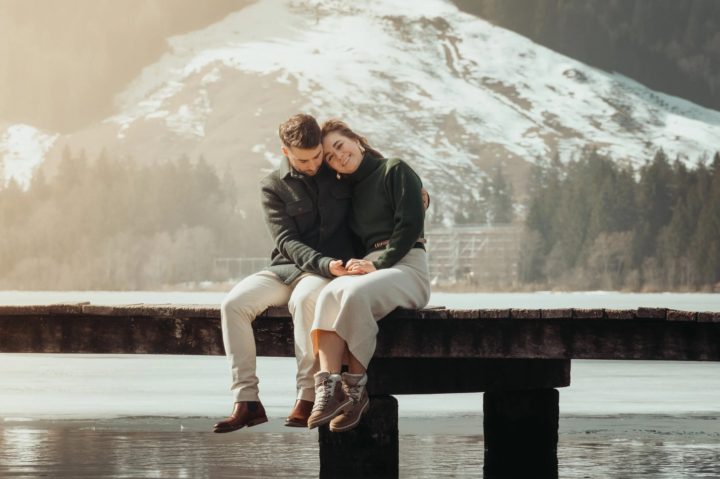 Un couple assis sur un banc en bois au bord d'un lac, entouré de montagnes enneigées, partageant un moment de tendresse et de bonheur.