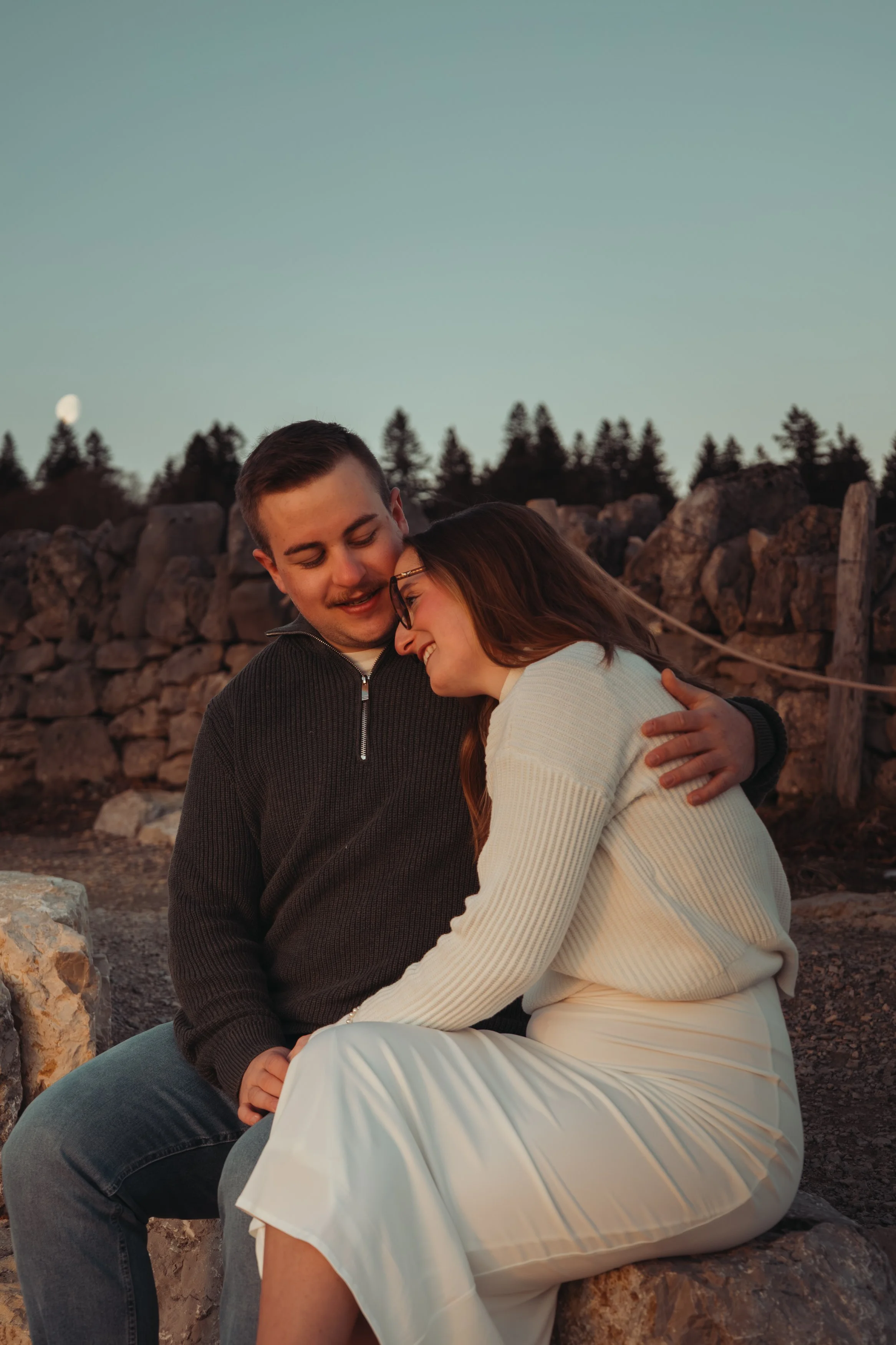 Un couple souriant et heureux, assis ensemble sur un rocher en plein air, partageant un moment intime au crépuscule.