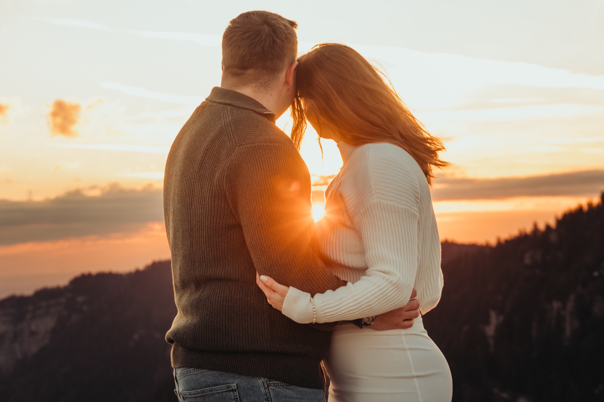 Un couple s'embrasse lors d'un coucher de soleil sur une colline avec une vue sur la mer, créant une scène romantique et paisible.