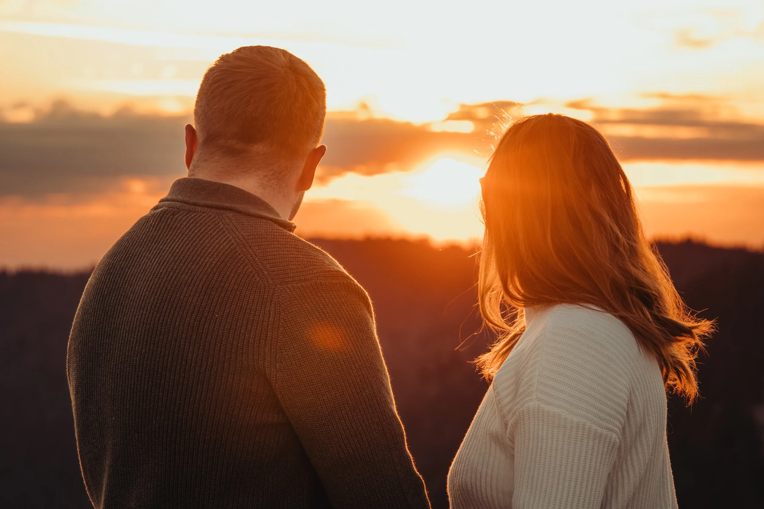 Deux personnes regardent un coucher de soleil, une homme et une femme, silhouettes visibles contre un ciel orange