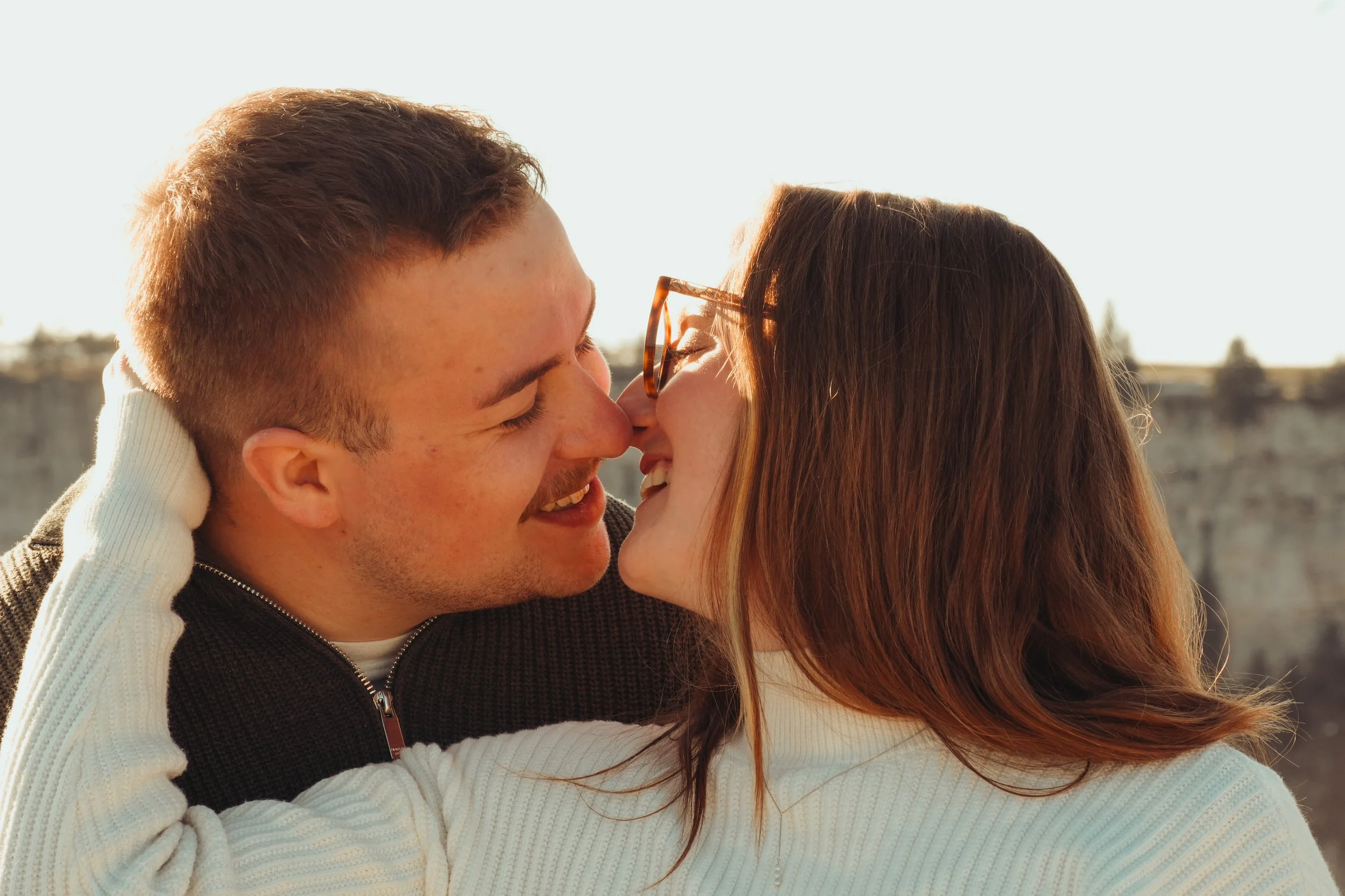 Un couple qui s'embrasse tendrement à l'extérieur, sous un ciel clair.