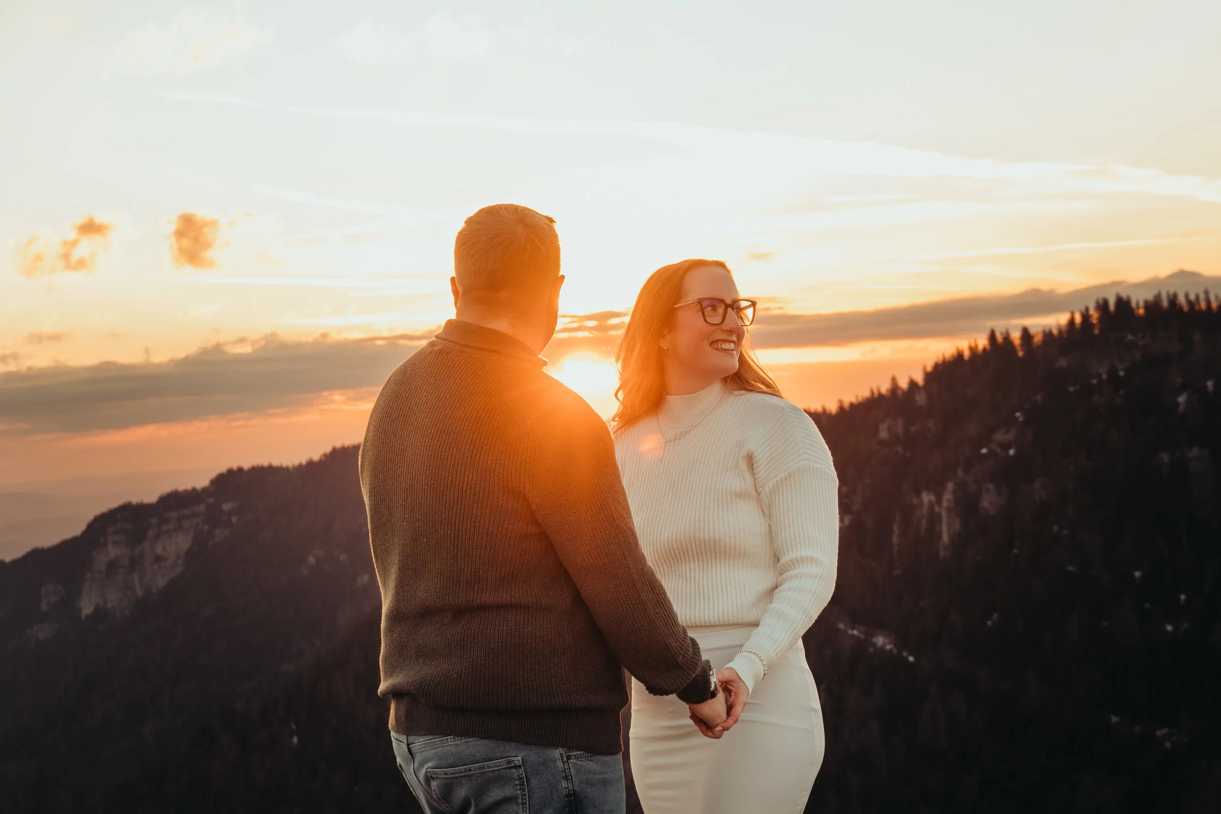Un couple regardant le coucher du soleil dans un paysage montagneux, se tenant la main.