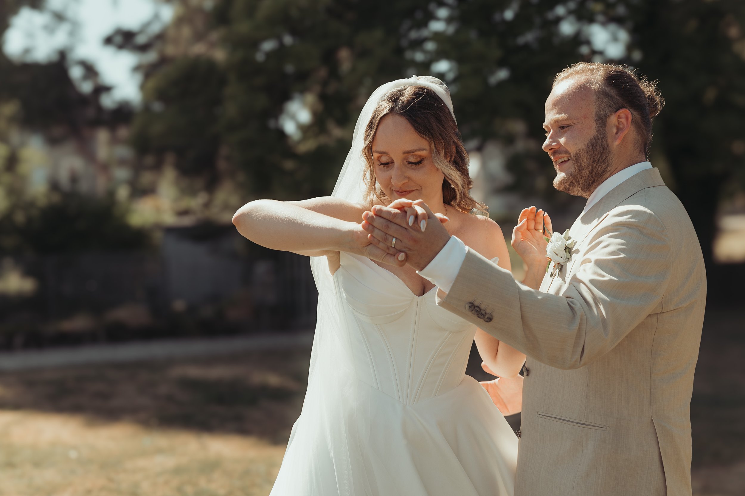 Un couple en mariée et marié lors d'une cérémonie en plein air, échangeant des bagues de mariage, avec un fond naturel d'arbres et de lumière naturelle.