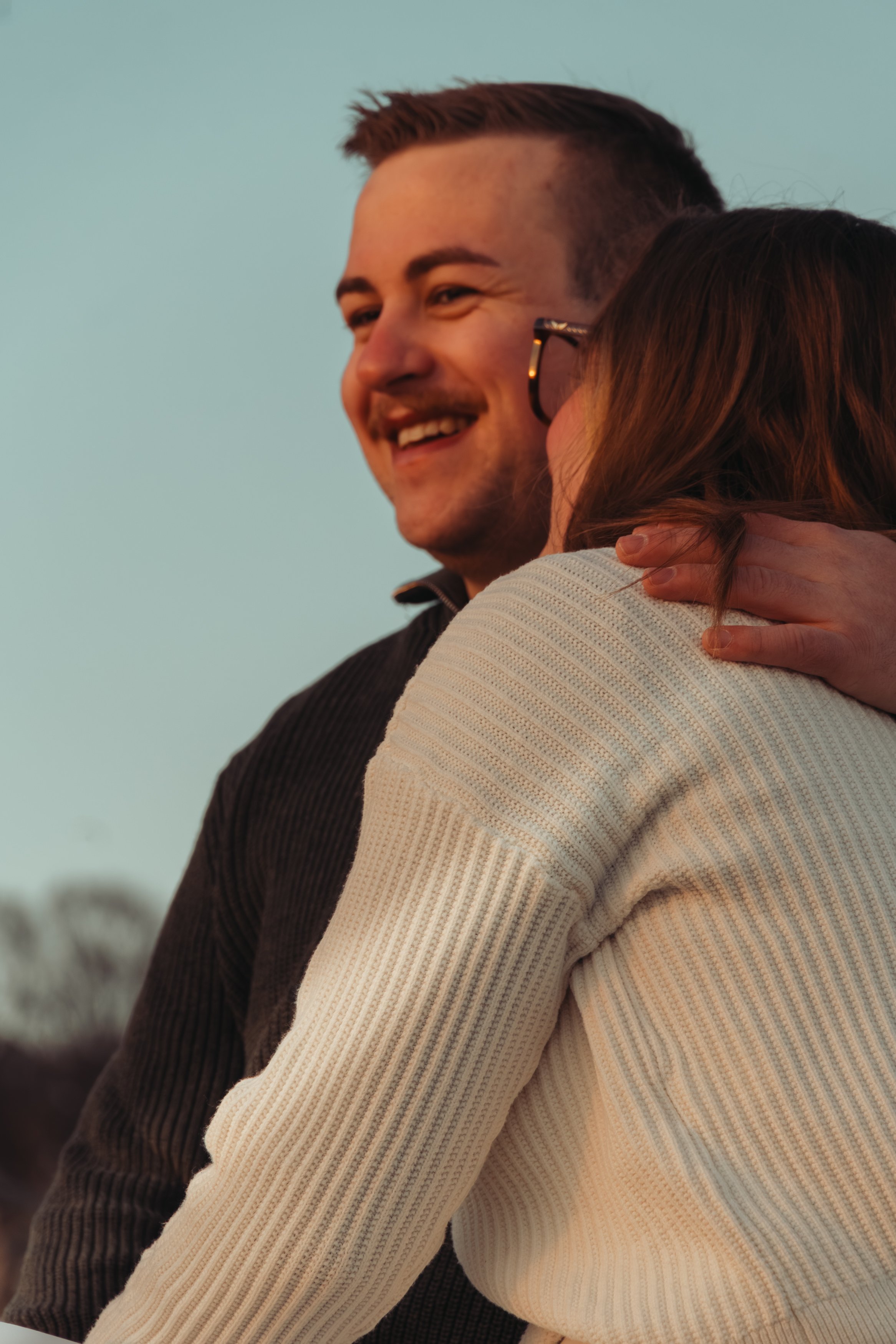 Un homme et une femme s'étreignent et sourient, avec un ciel clair en arrière-plan.