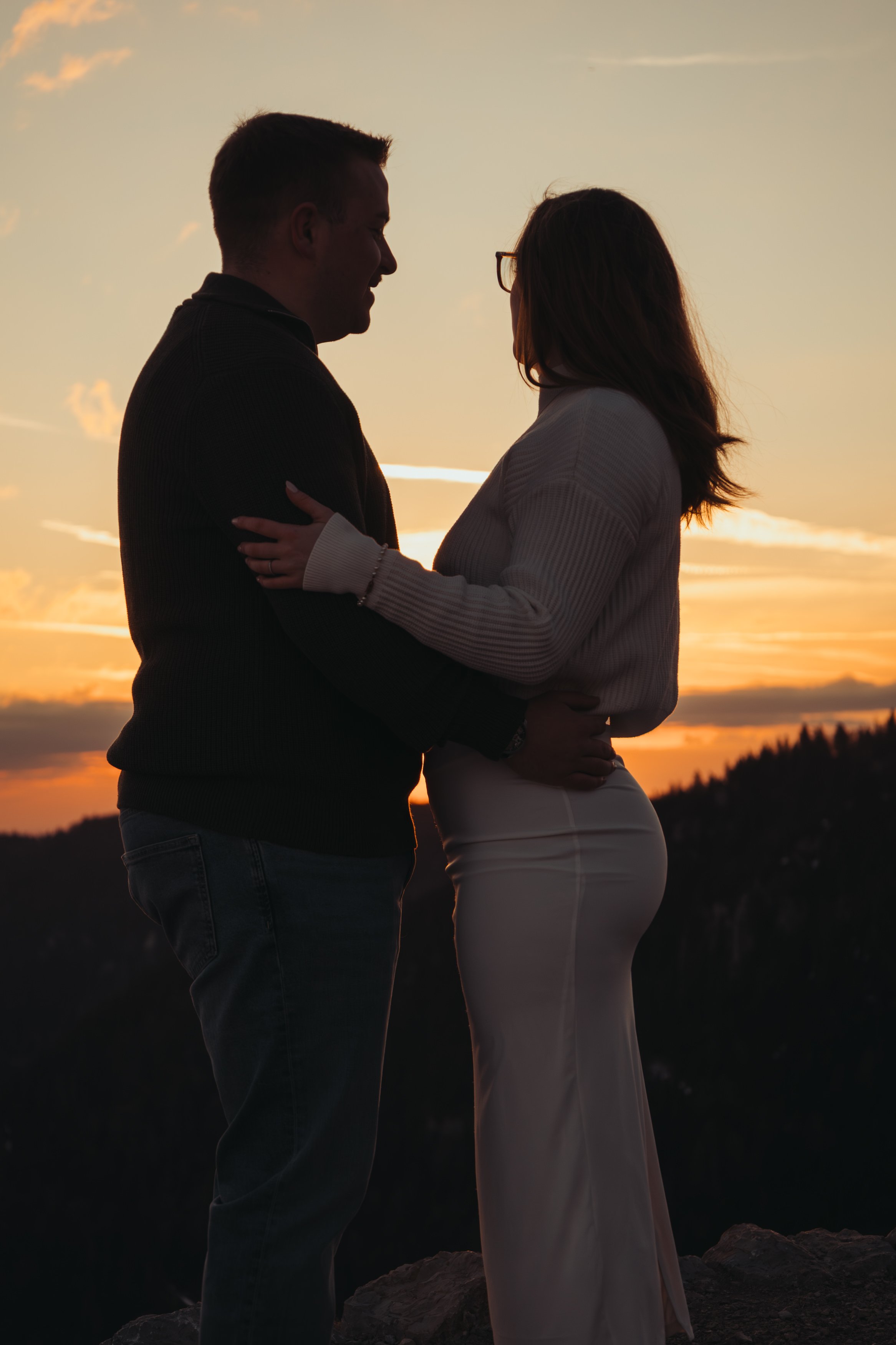 Un couple se tient face à face lors d'un coucher de soleil, en équilibre sur un rocher dans la nature.