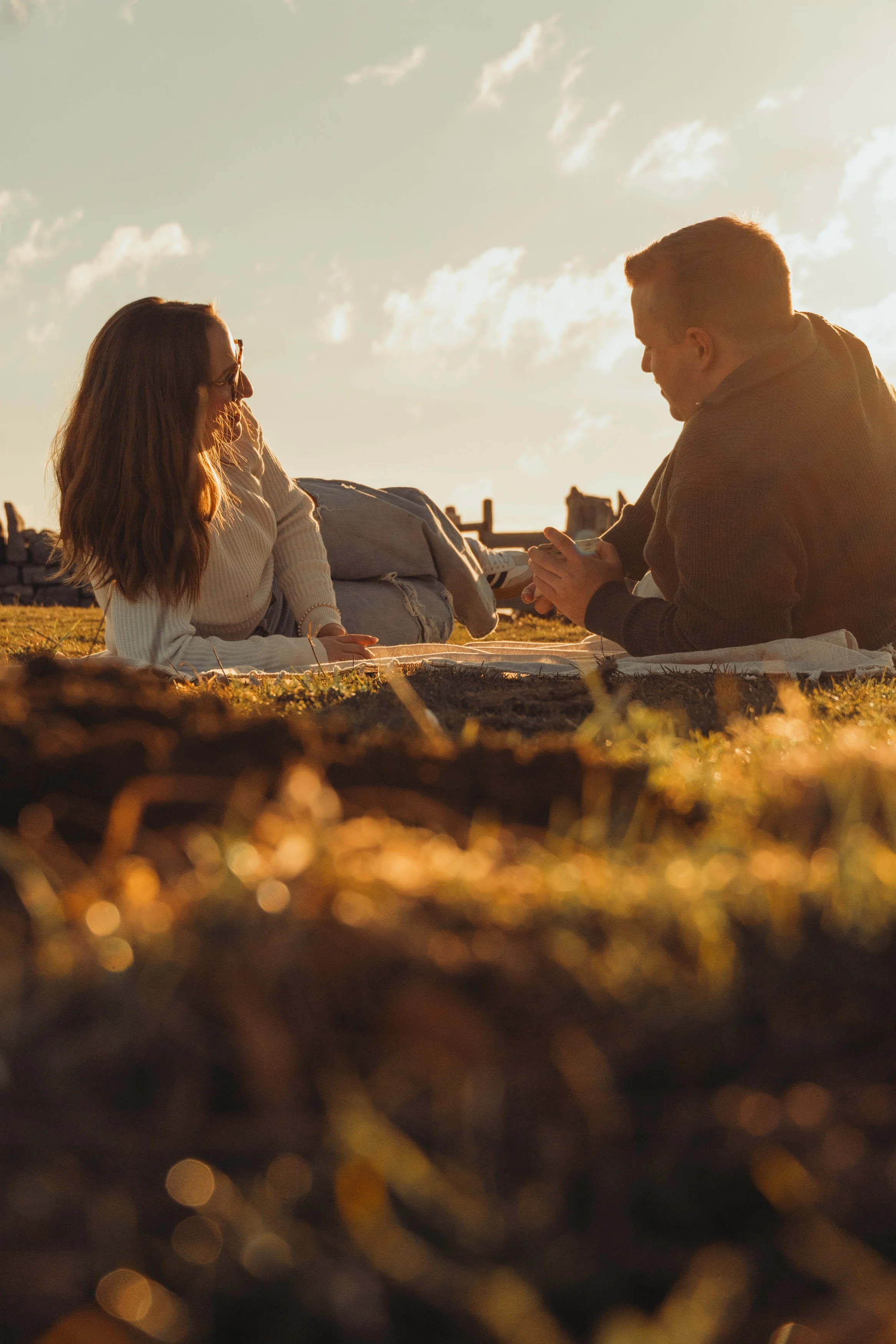 Deux personnes, un homme et une femme, assises sur l'herbe lors d'un coucher de soleil, discutant avec douceur.