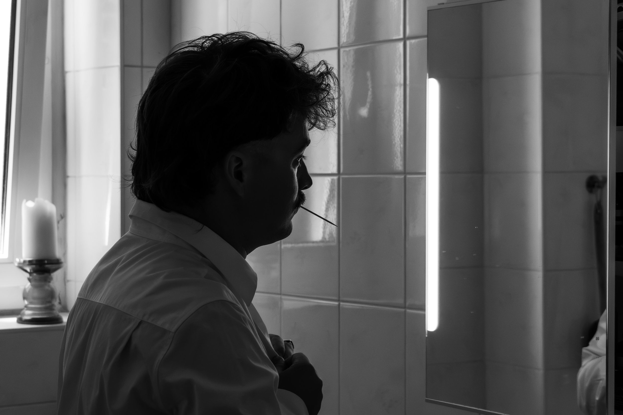 Un homme en profil, en train de se brosser les dents dans une salle de bain. L'image est en noir et blanc.