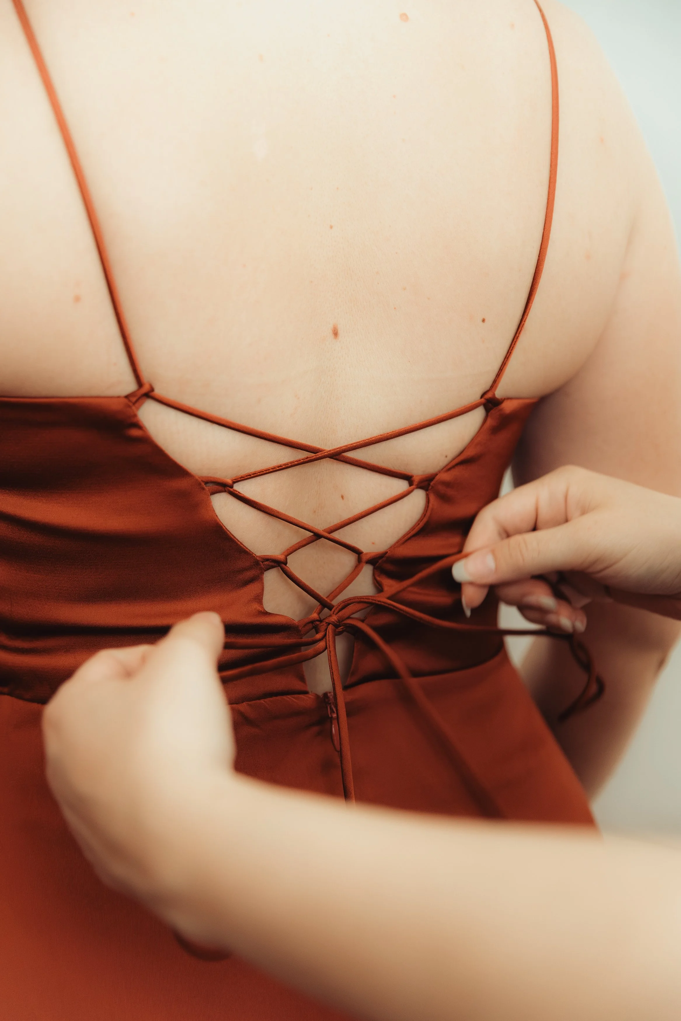 Un close-up du décolleté d'une femme portant une robe en satin marron avec des lacets croisés au centre. Une main ajustant la robe.