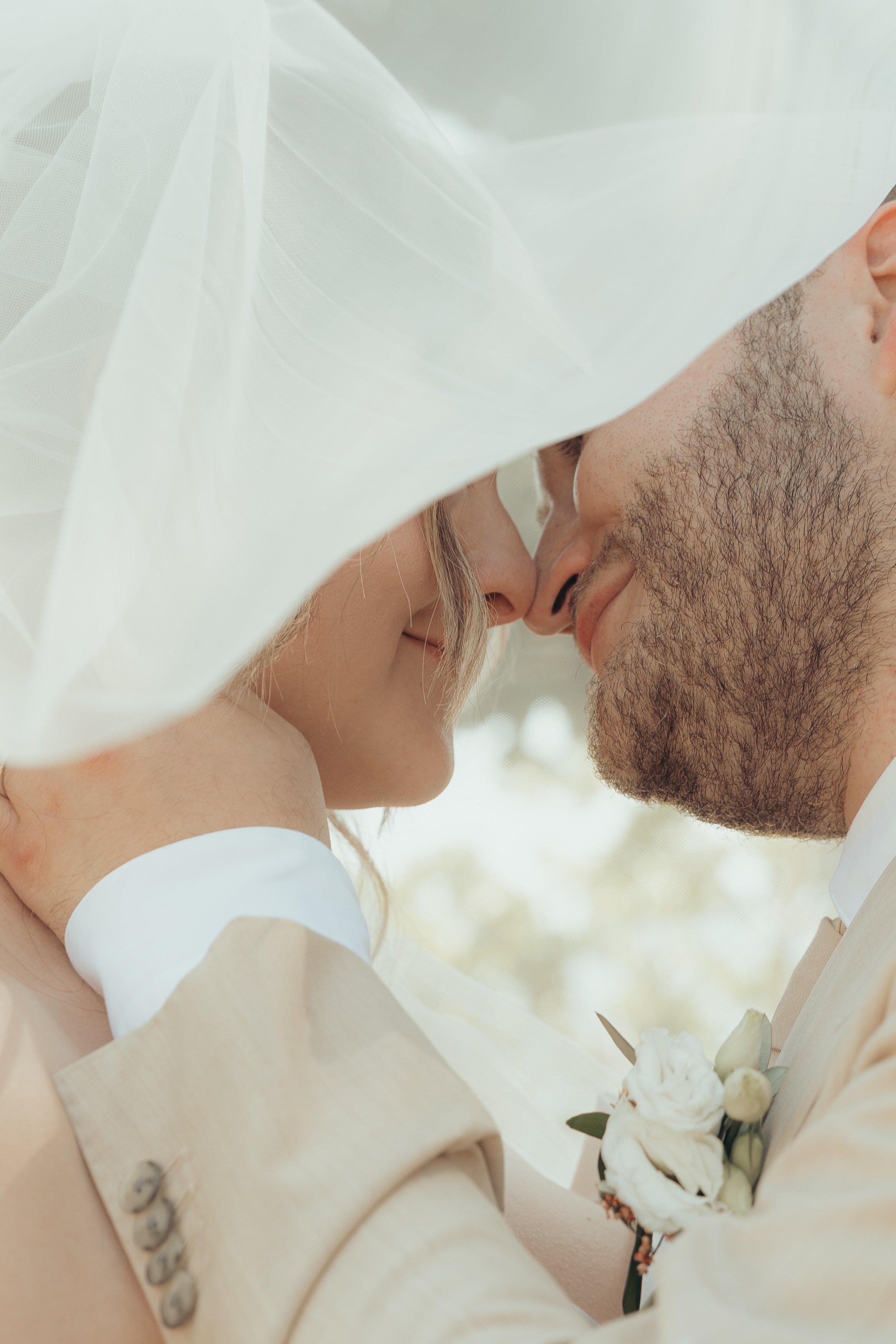 Un couple de mariés s'embrassant sous un voile de mariée blanc, avec un bouquet de fleurs blanches.
