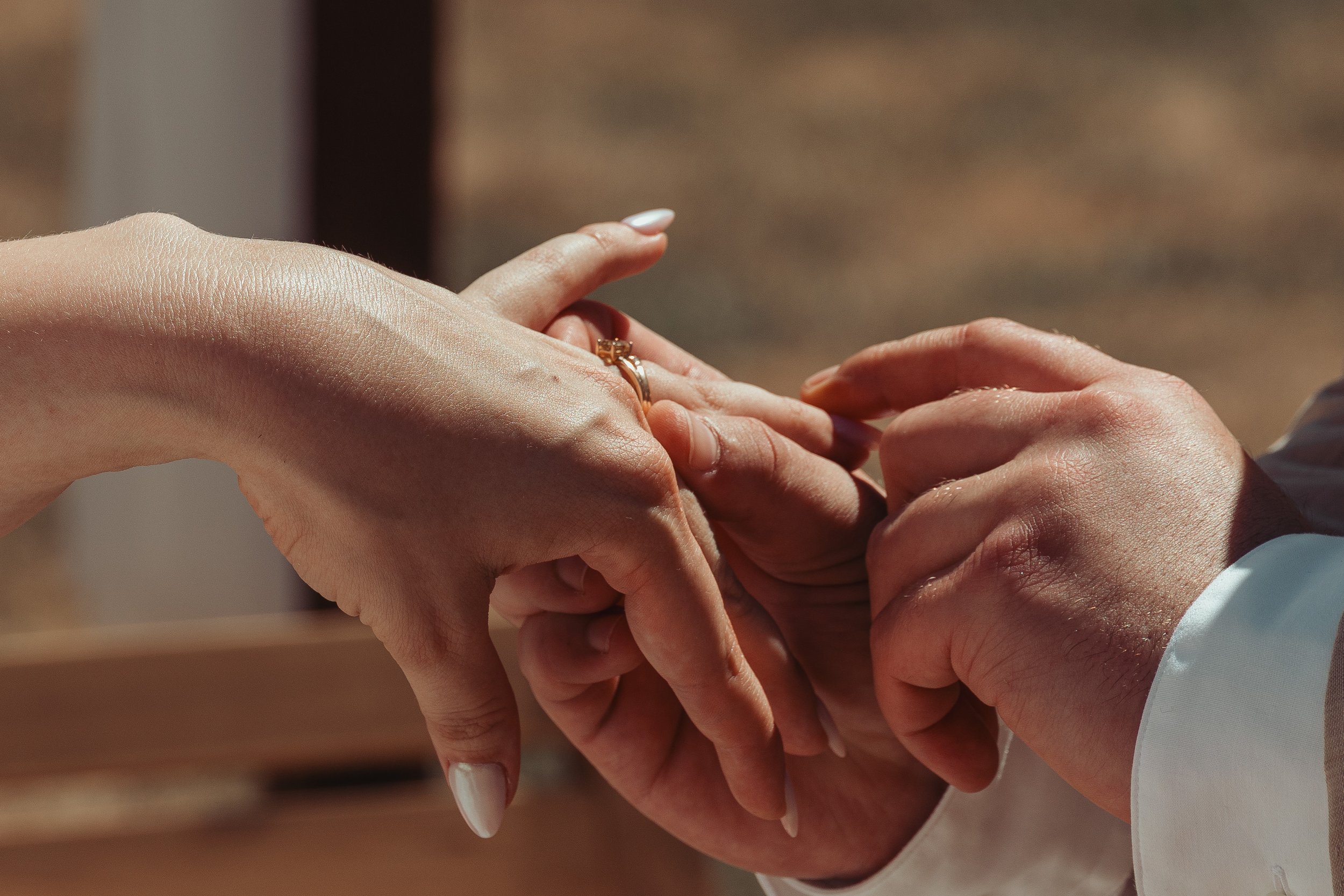 Deux mains qui échangent des alliances, l'une portant une bague en or avec un diamant. Contexte de mariage ou d'engagement.