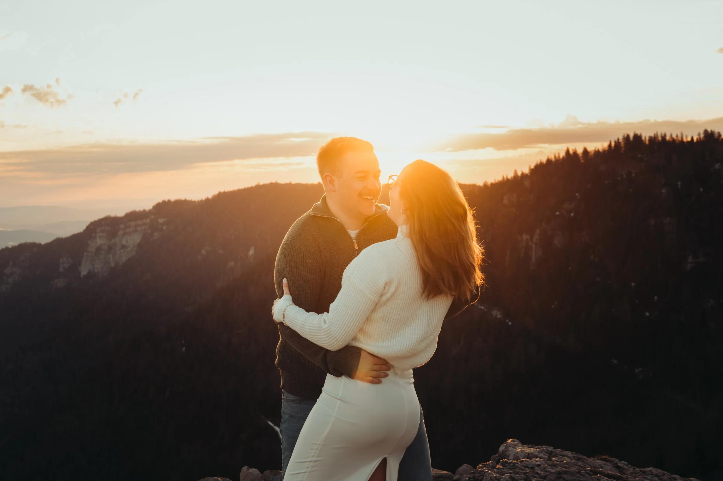 Un couple souriant s'enlace lors d'un coucher de soleil dans une région montagneuse.