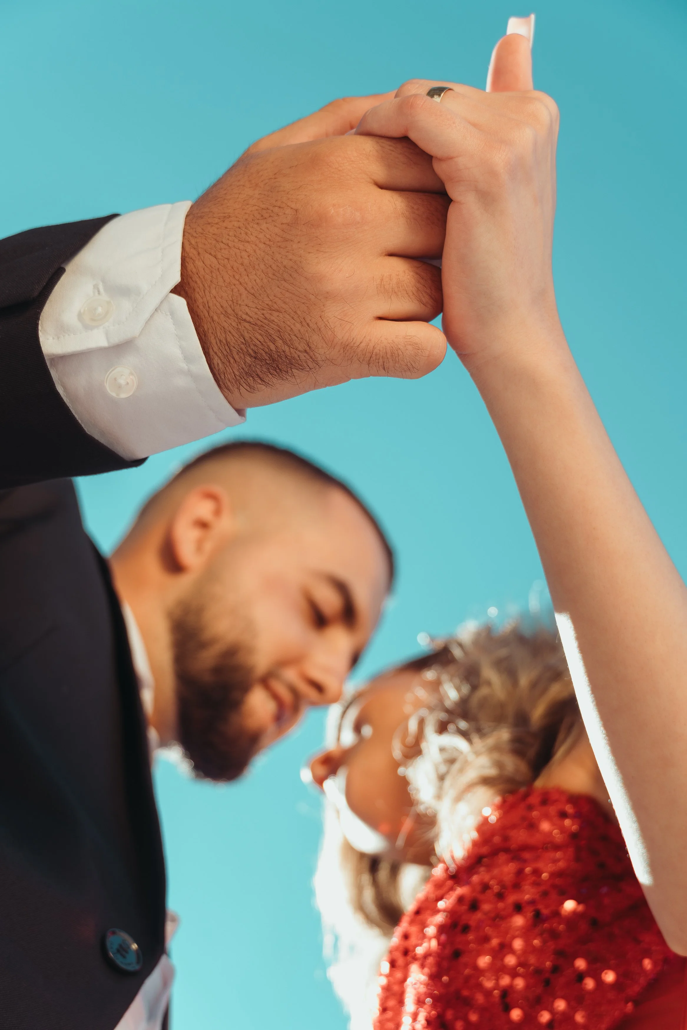 Un couple s'embrasse lors d'une cérémonie, tenant leurs mains entre elles, avec un fond bleu clair lors d'une séance fiançailles avec Marie Monod photographe d'émotions, duo de photographes queer en Suisse.