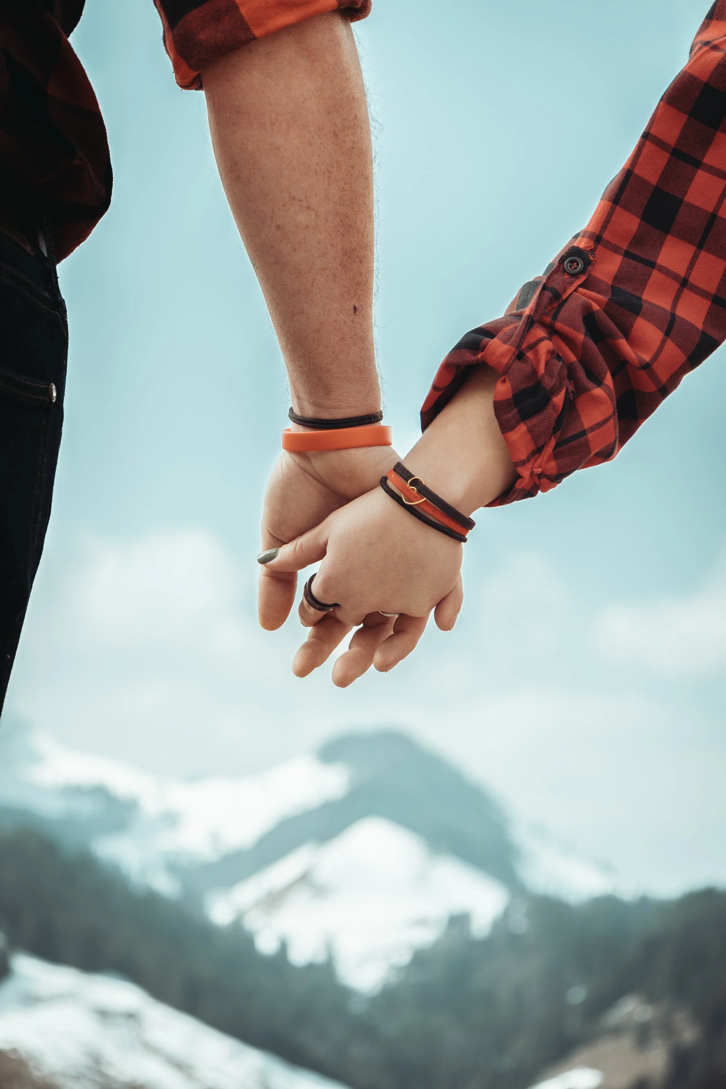 Deux personnes tenant la main contre un paysage de montagnes avec des sommets enneigés et un ciel nuageux.