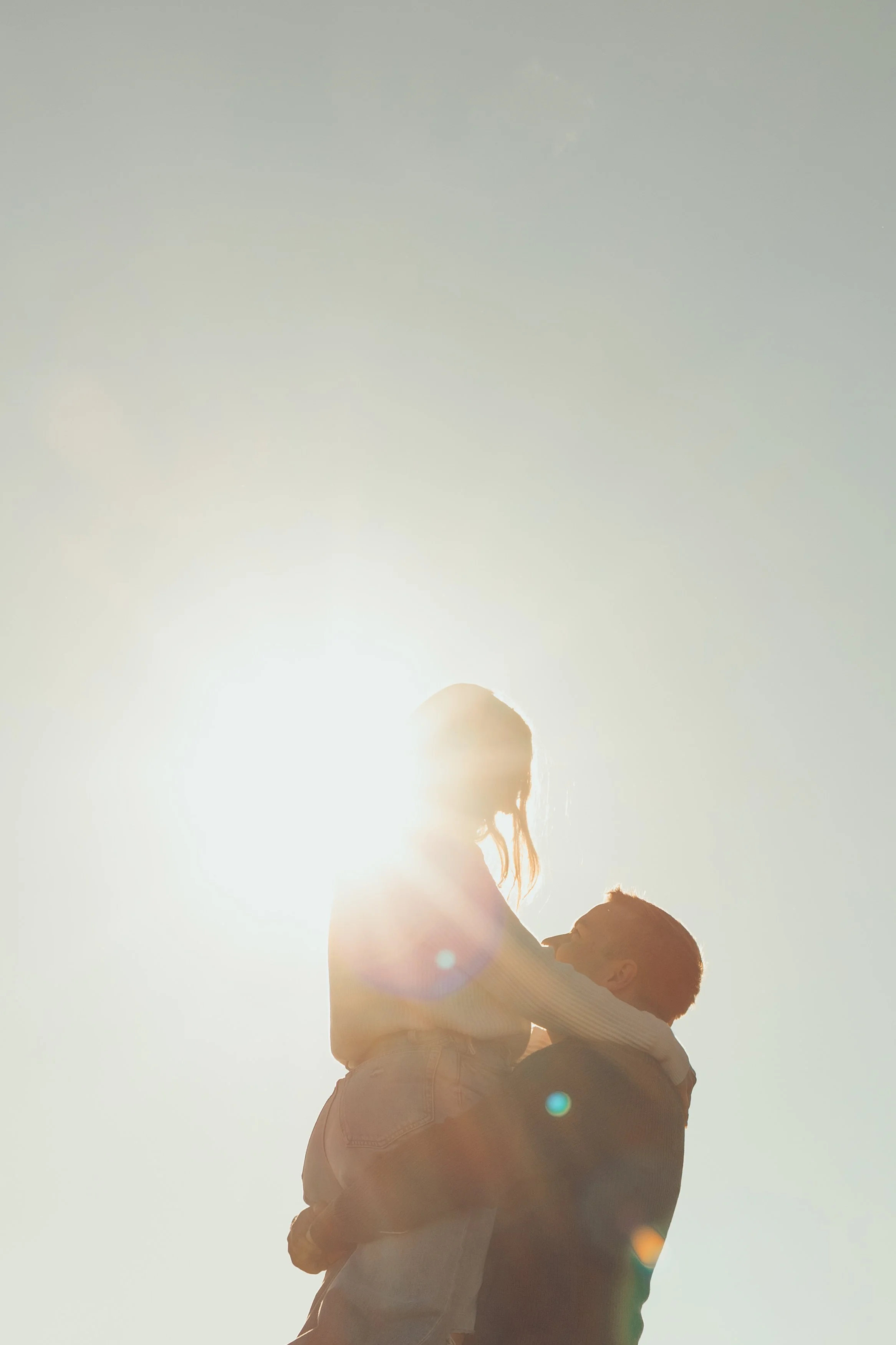 Un adulte et un enfant jouent ensemble avec le soleil en arrière-plan, créant un effet de silhouette lumineuse.