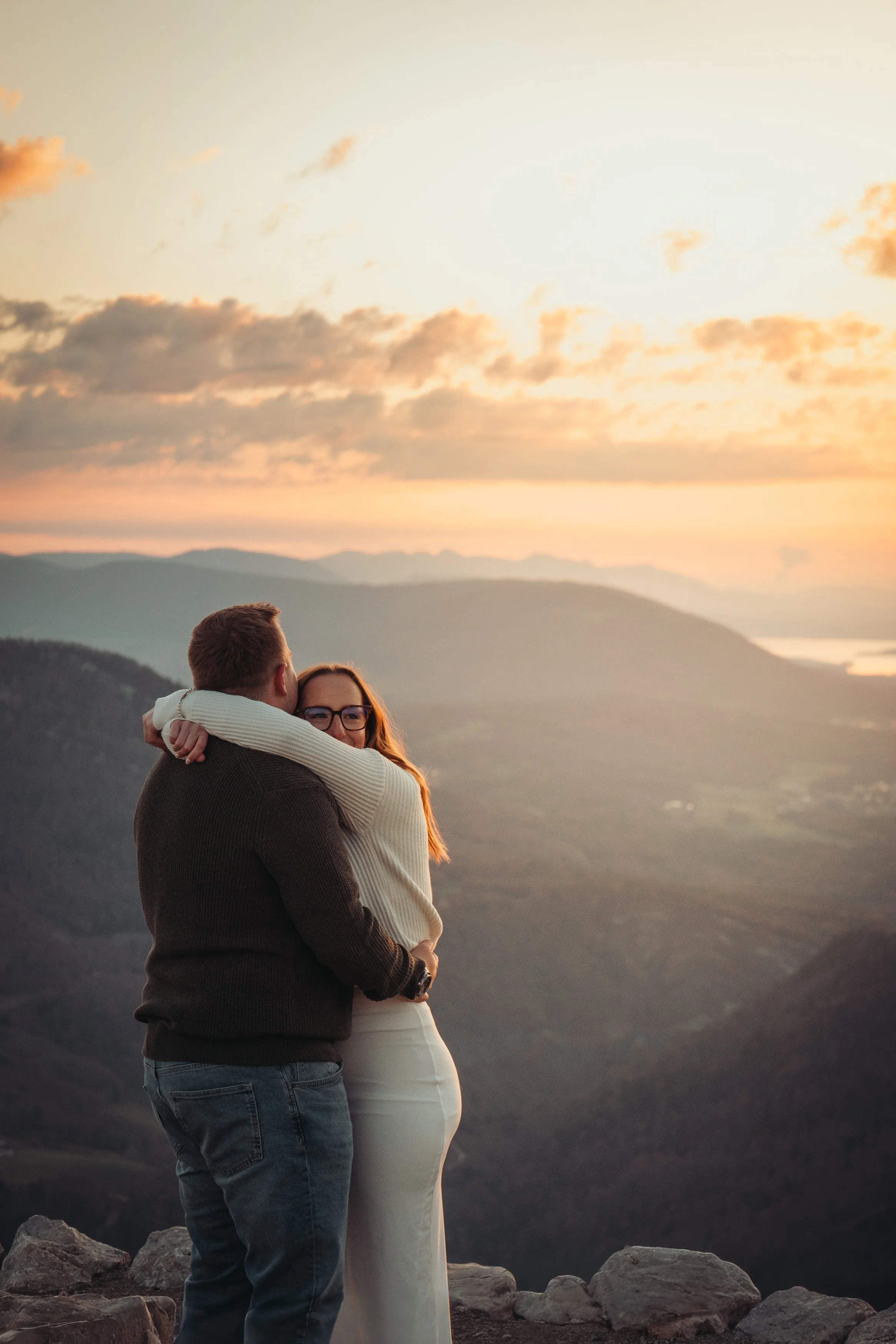 Un couple s'embrasse face à un paysage montagneux au coucher du soleil.