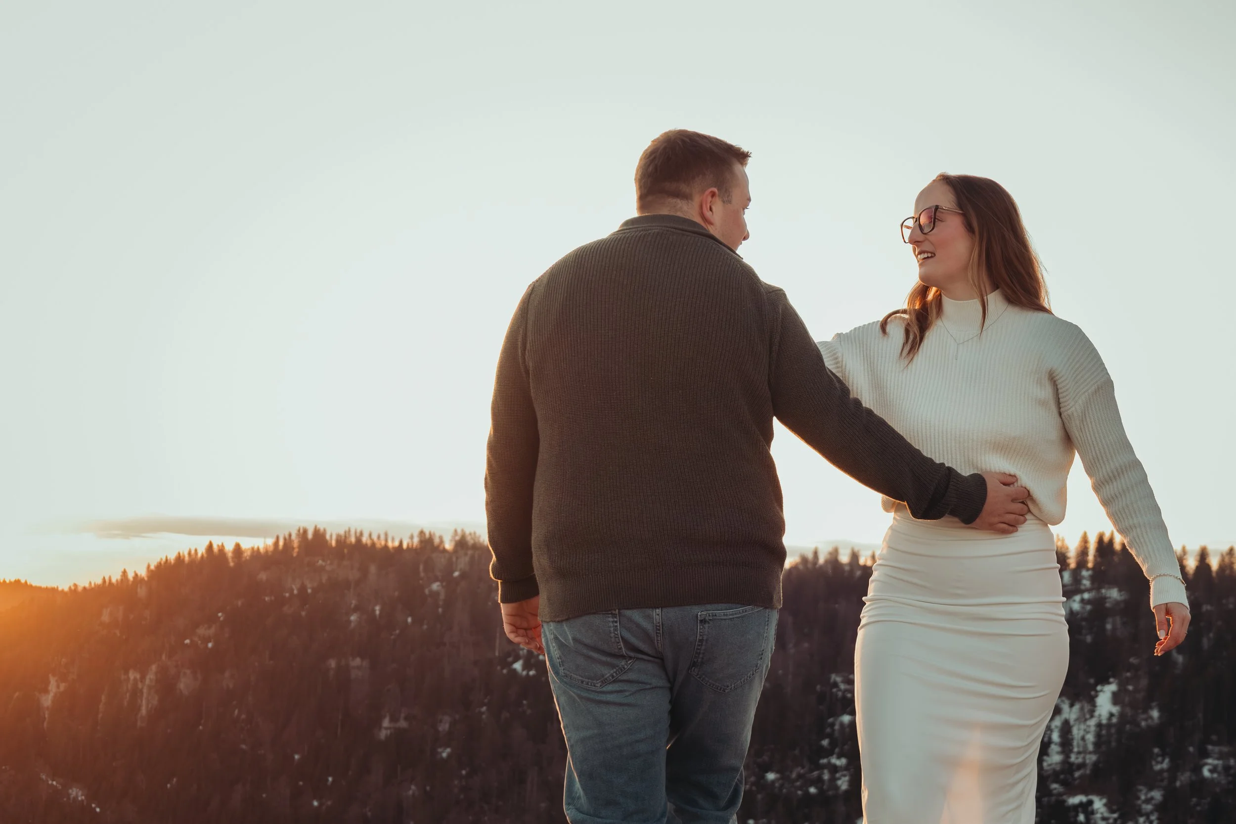 Un couple marche ensemble dans un paysage naturel avec un coucher de soleil en arrière-plan, partageant un moment de complicité et de bonheur.