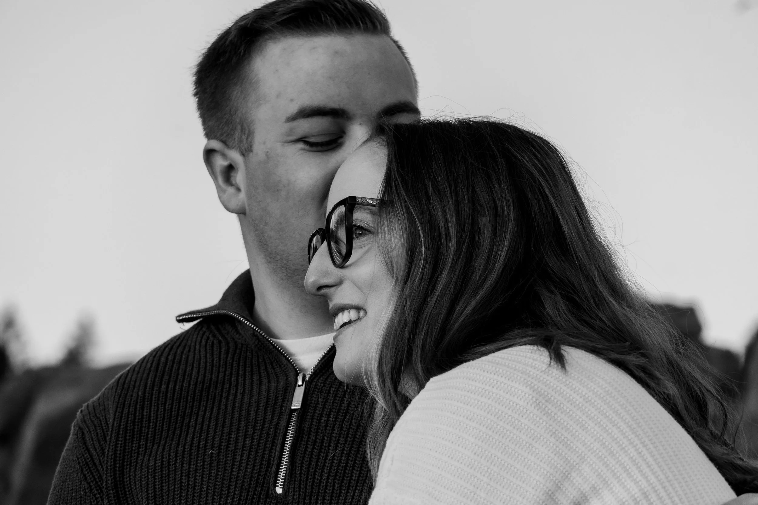 Un jeune couple partage un moment affectueux, le garçon embrasse la fille sur la tête, tous deux souriants et visibles en gros plan.