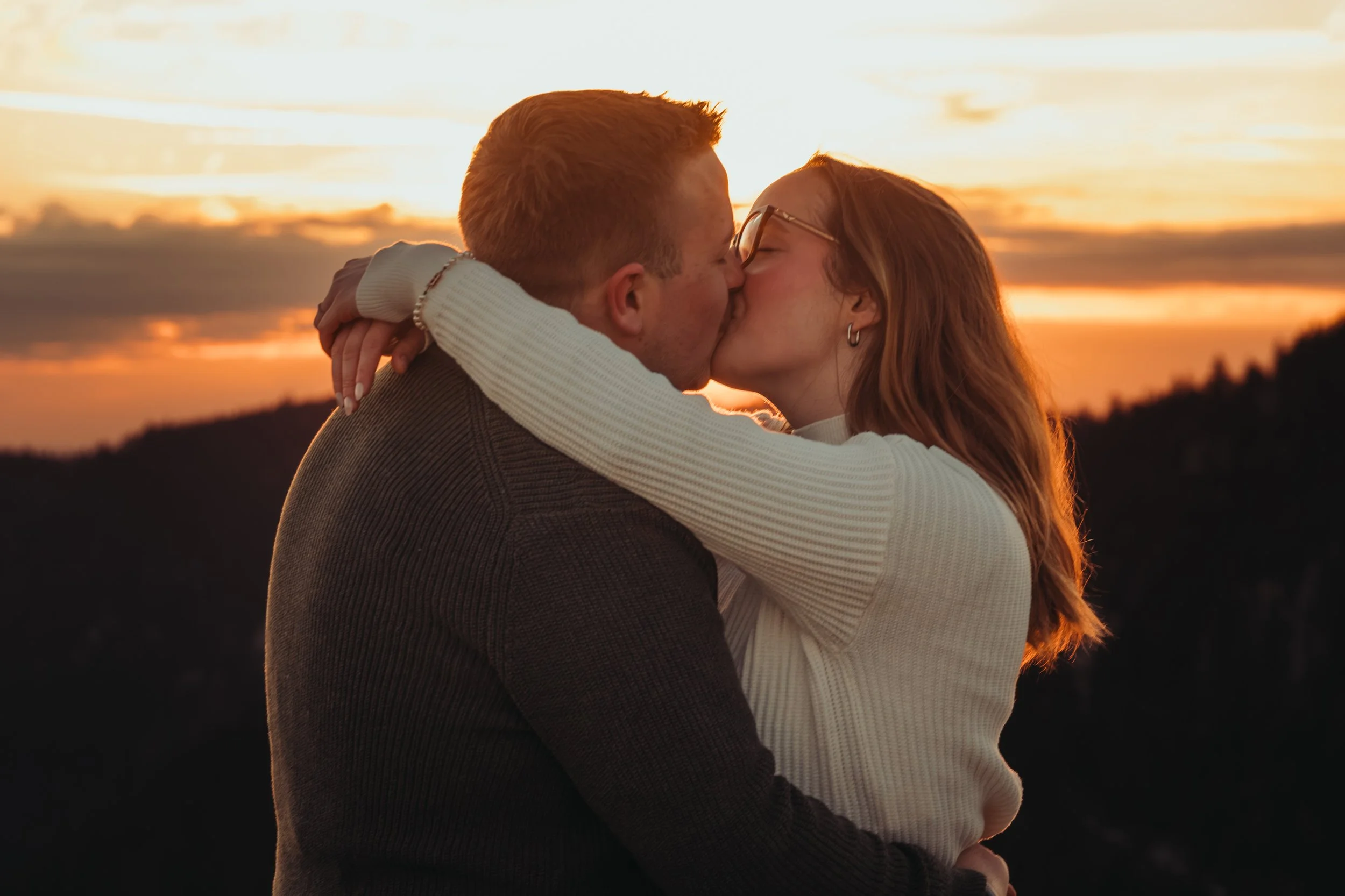 Un couple s'embrasse tendrement lors d'un coucher de soleil, avec le ciel orange en arrière-plan.