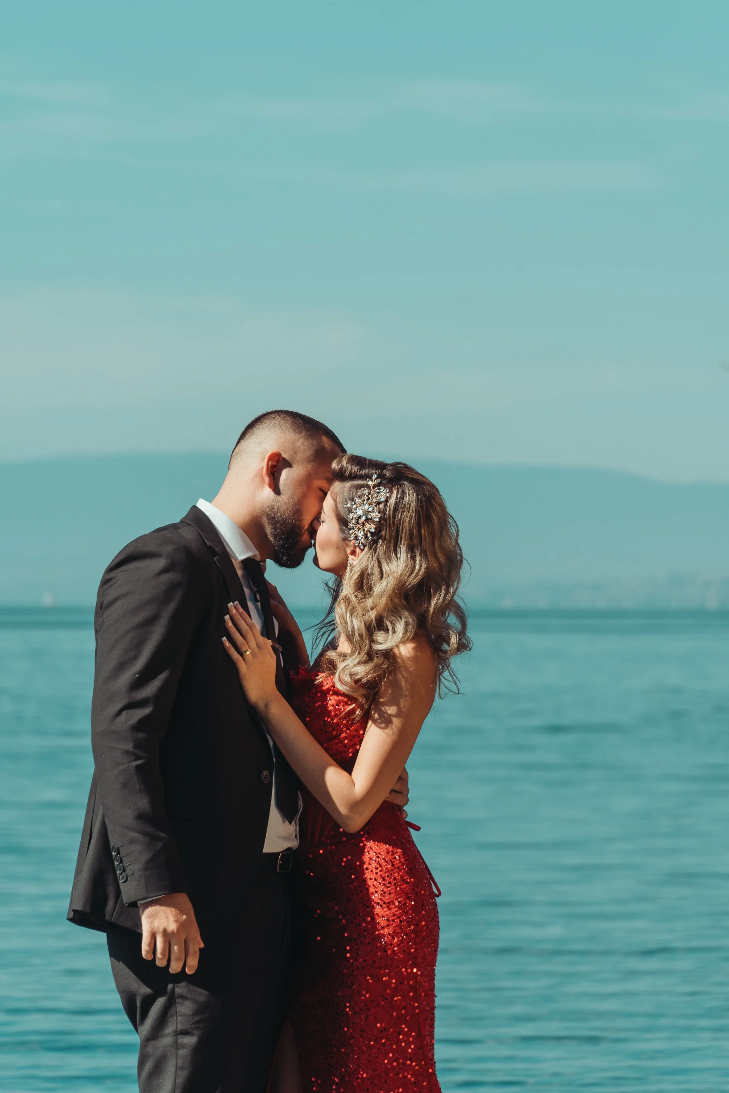 un couple en habits de mariage s'embrassant près de l'eau, dans un décor en plein air avec un ciel bleu lors d'une séance couple avec Marie Monod photographe d'émotions, duo de photographes queer en Suisse au lac léman