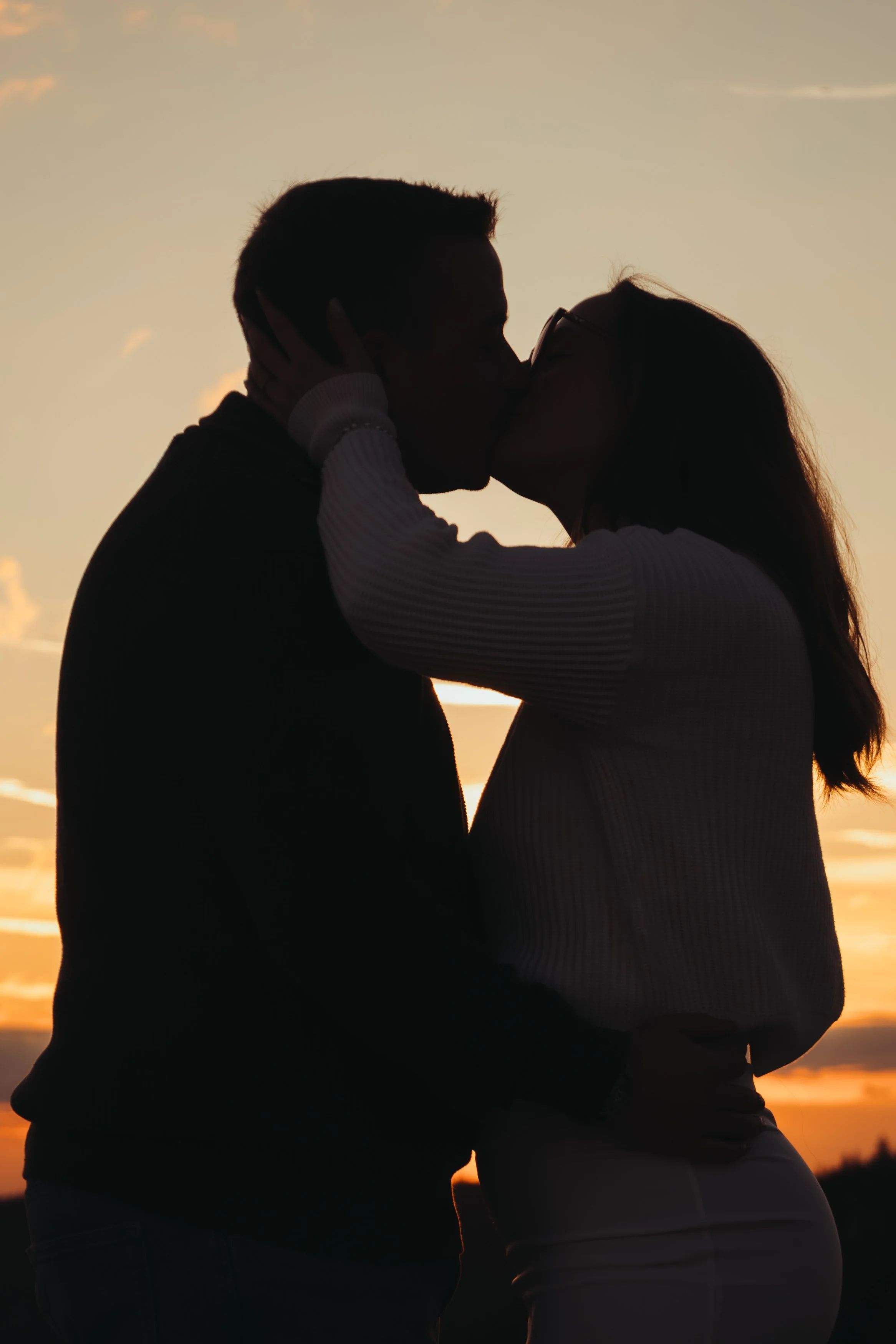 Un couple s'embrasse lors d'un coucher de soleil, silhouette sombre contre un ciel orange.