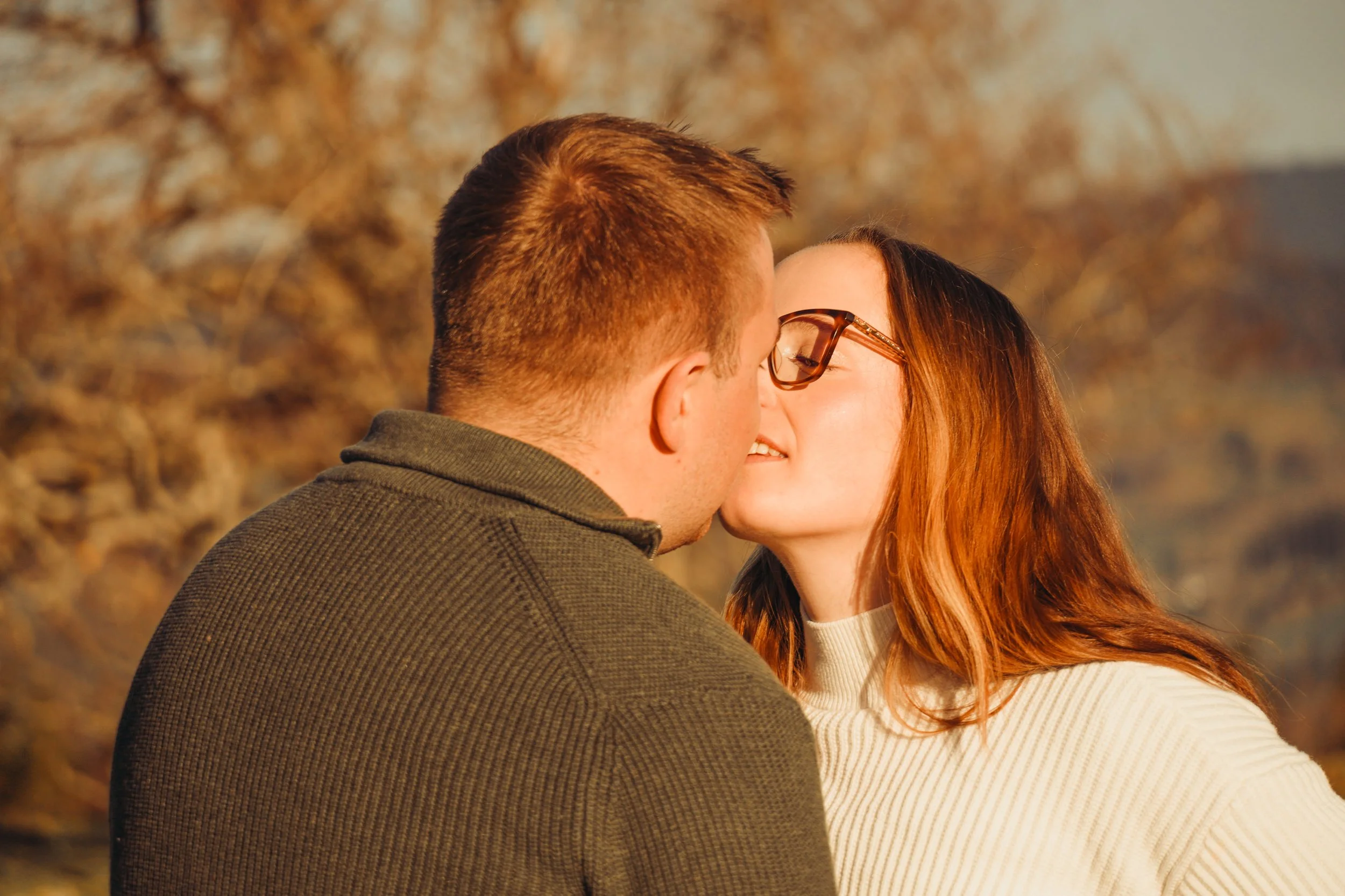 Un couple s'embrasse tendrement dans un parc en automne, entouré d'arbres aux feuilles dorées.