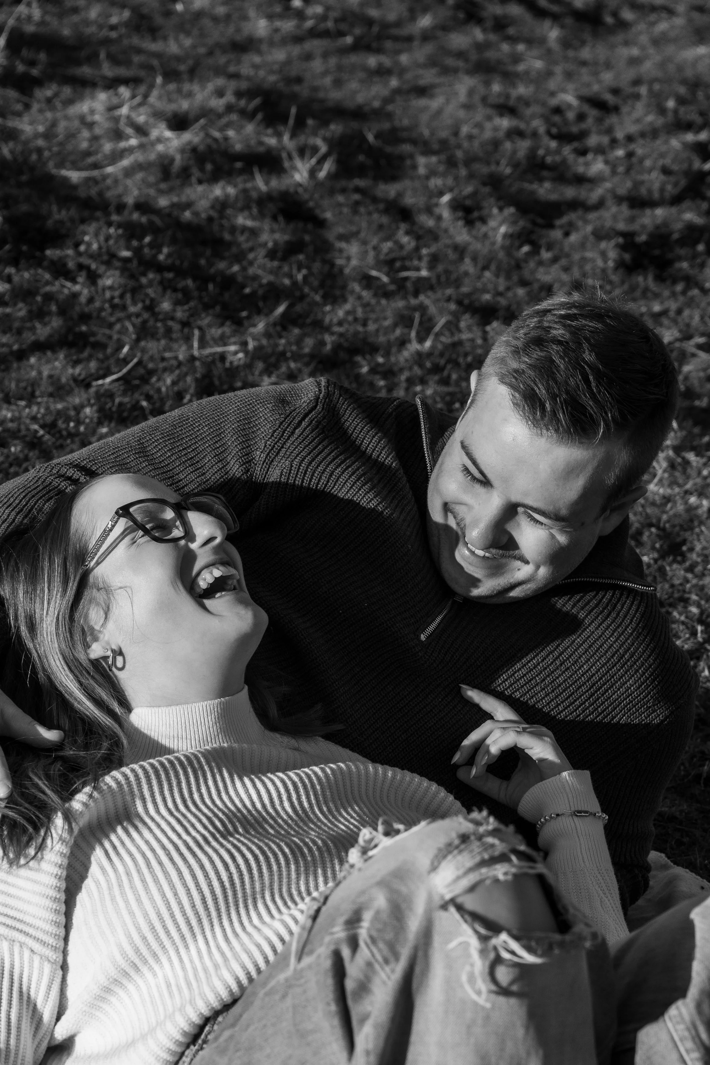 Deux personnes, un homme et une femme, allongés sur le sol en pleine nature, souriants et riant ensemble.