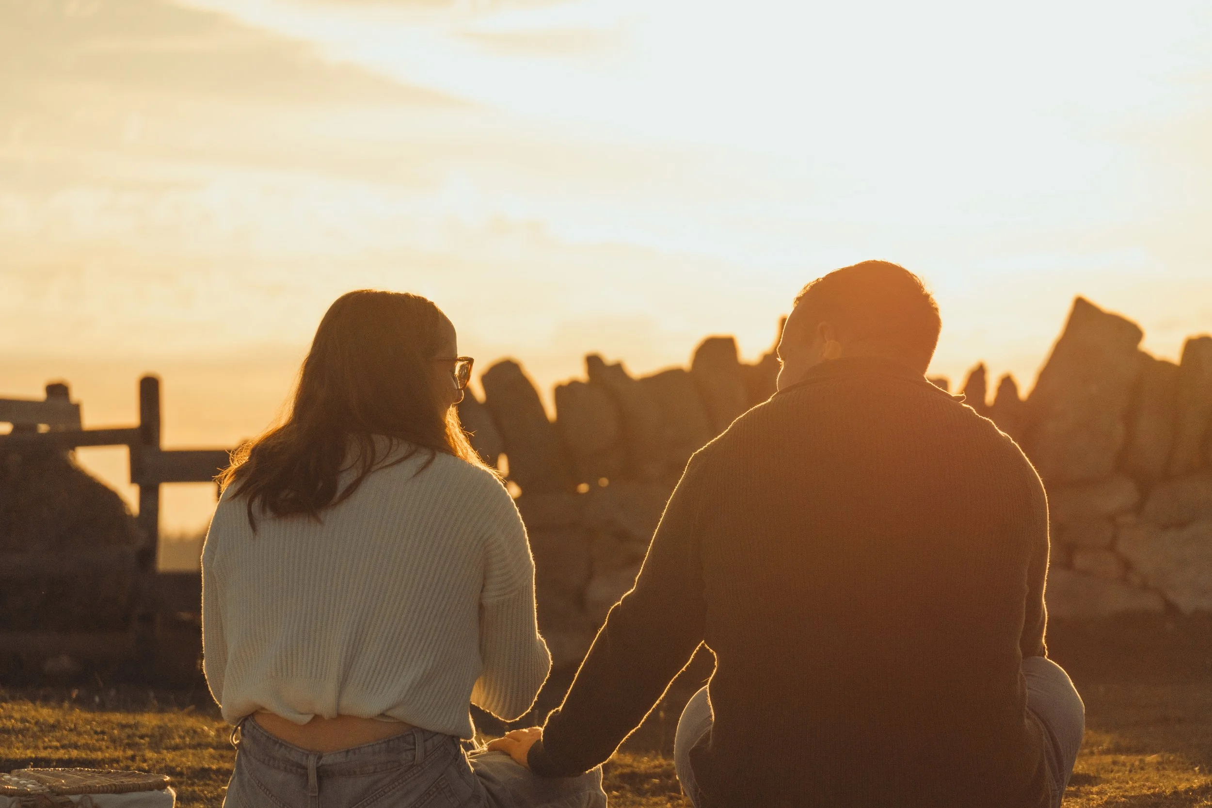 Deux personnes assises côte à côte en regardant le coucher de soleil, avec un paysage rocheux en arrière-plan.