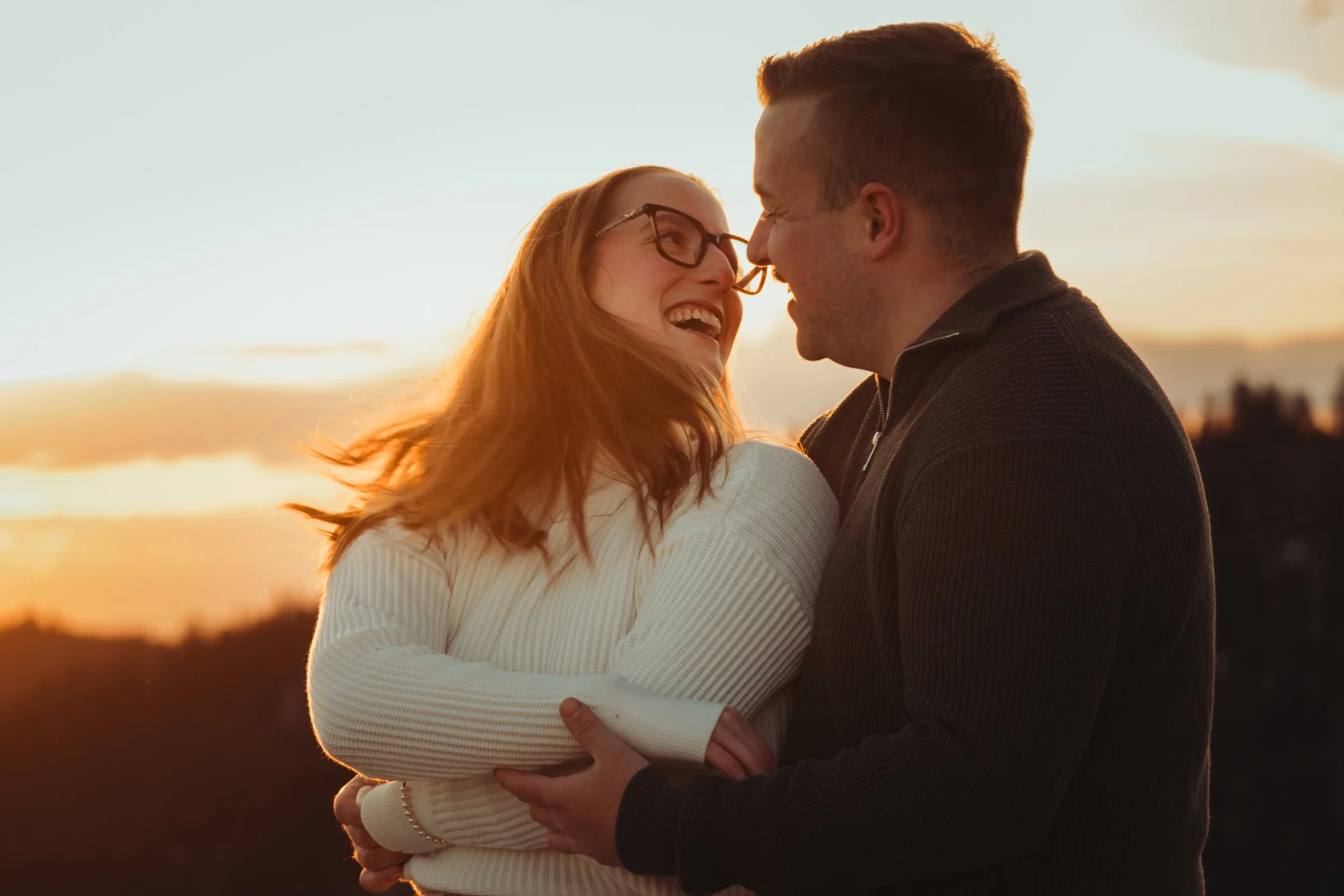 Un couple souriant en se regardant près d'un coucher de soleil, avec la mer en arrière-plan.