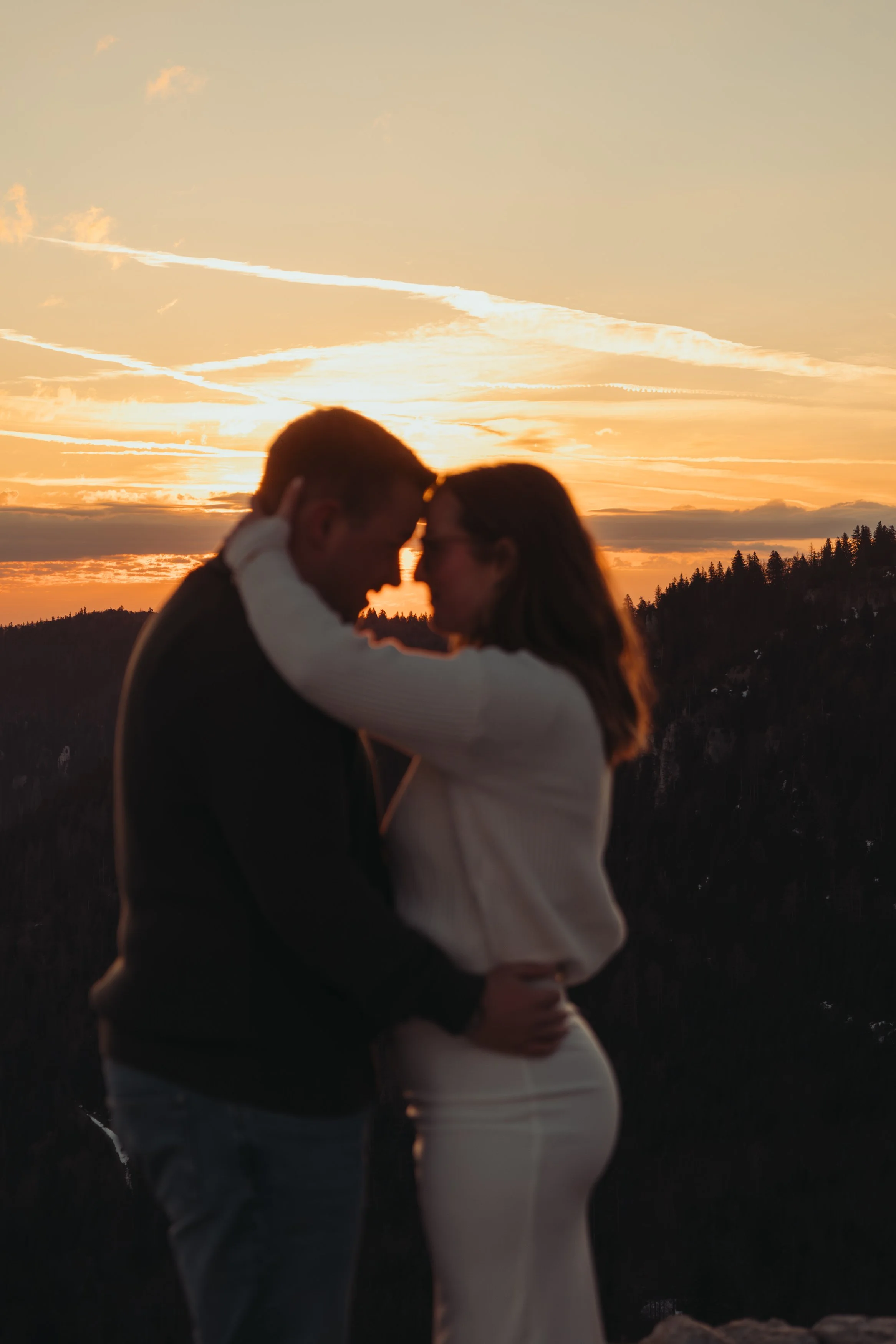 Un couple qui s'embrasse lors d'un coucher de soleil, avec un ciel orangé et des nuages.