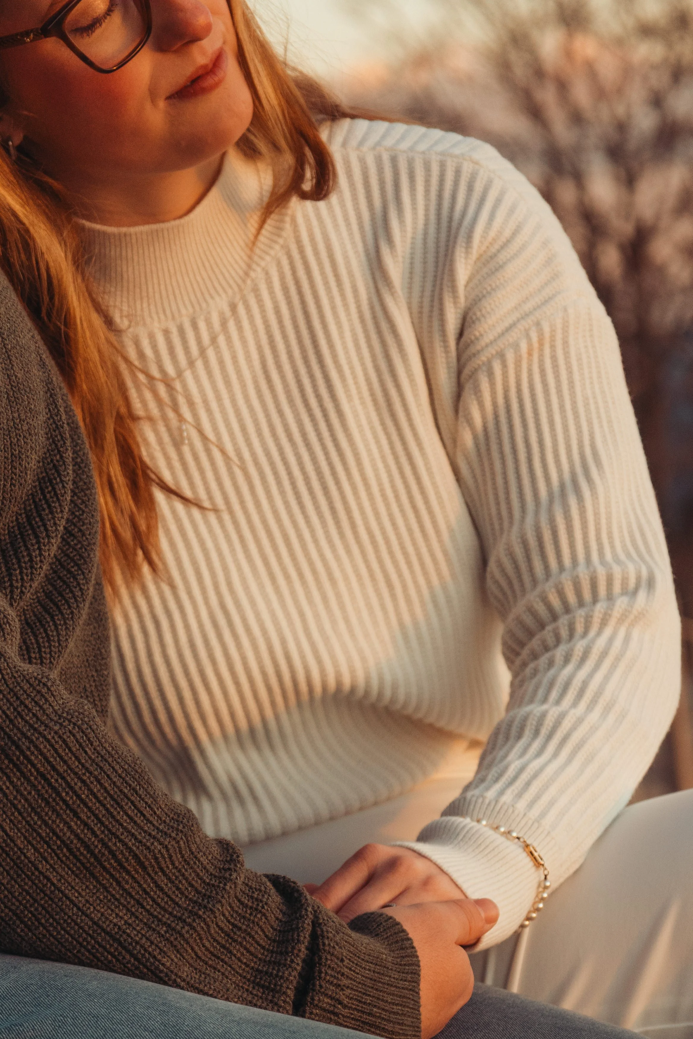 Deux personnes, une avec un pull blanc à rayures et l'autre avec un pull marron à texture côtelée, assises côte à côte, les mains croisées, dans un cadre intérieur.