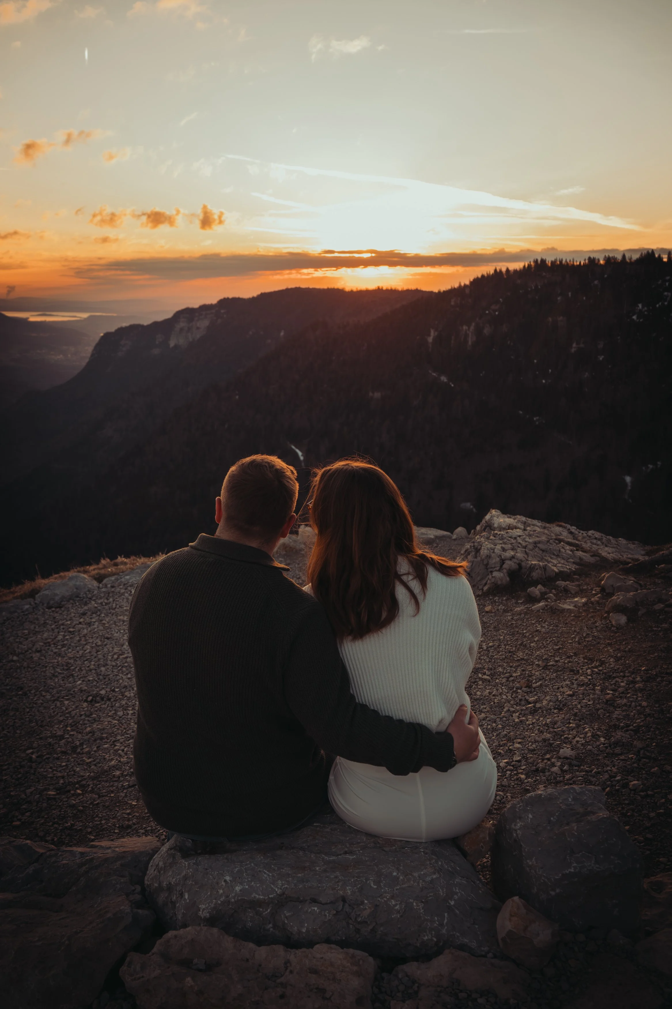 Un couple assis sur des rochers regardant un coucher de soleil sur des montagnes et la vallée au loin.