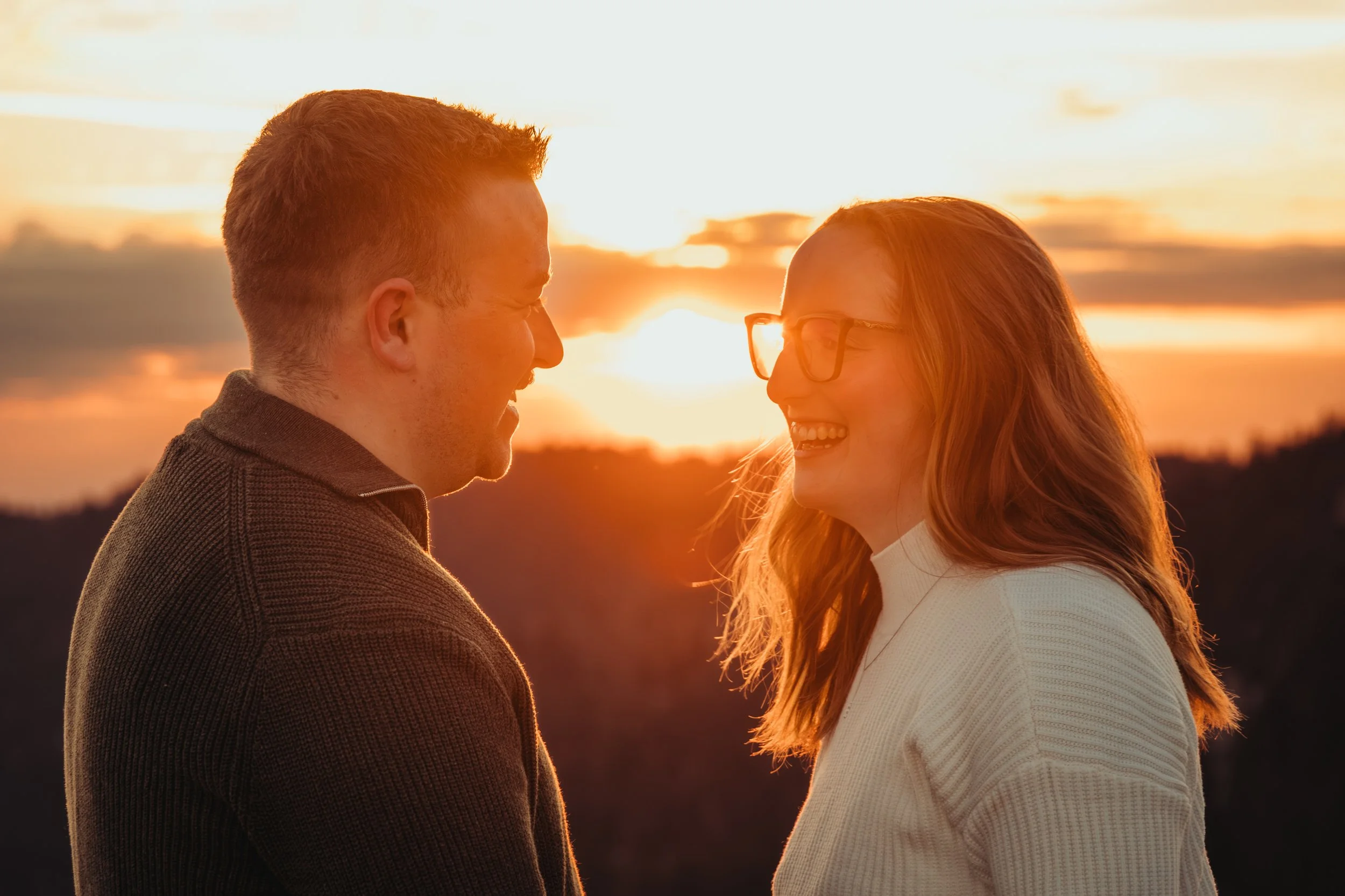 Un couple souriant face à face lors d'un coucher de soleil, créant une ambiance romantique.