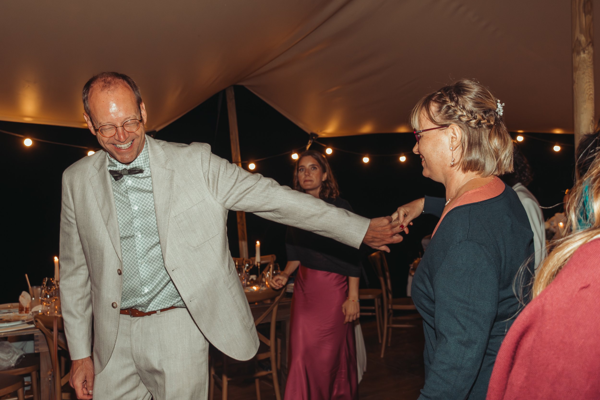Groupe de personnes dansant et souriant lors d'une fête en soirée sous un chapiteau éclairé par des guirlandes lumineuses.