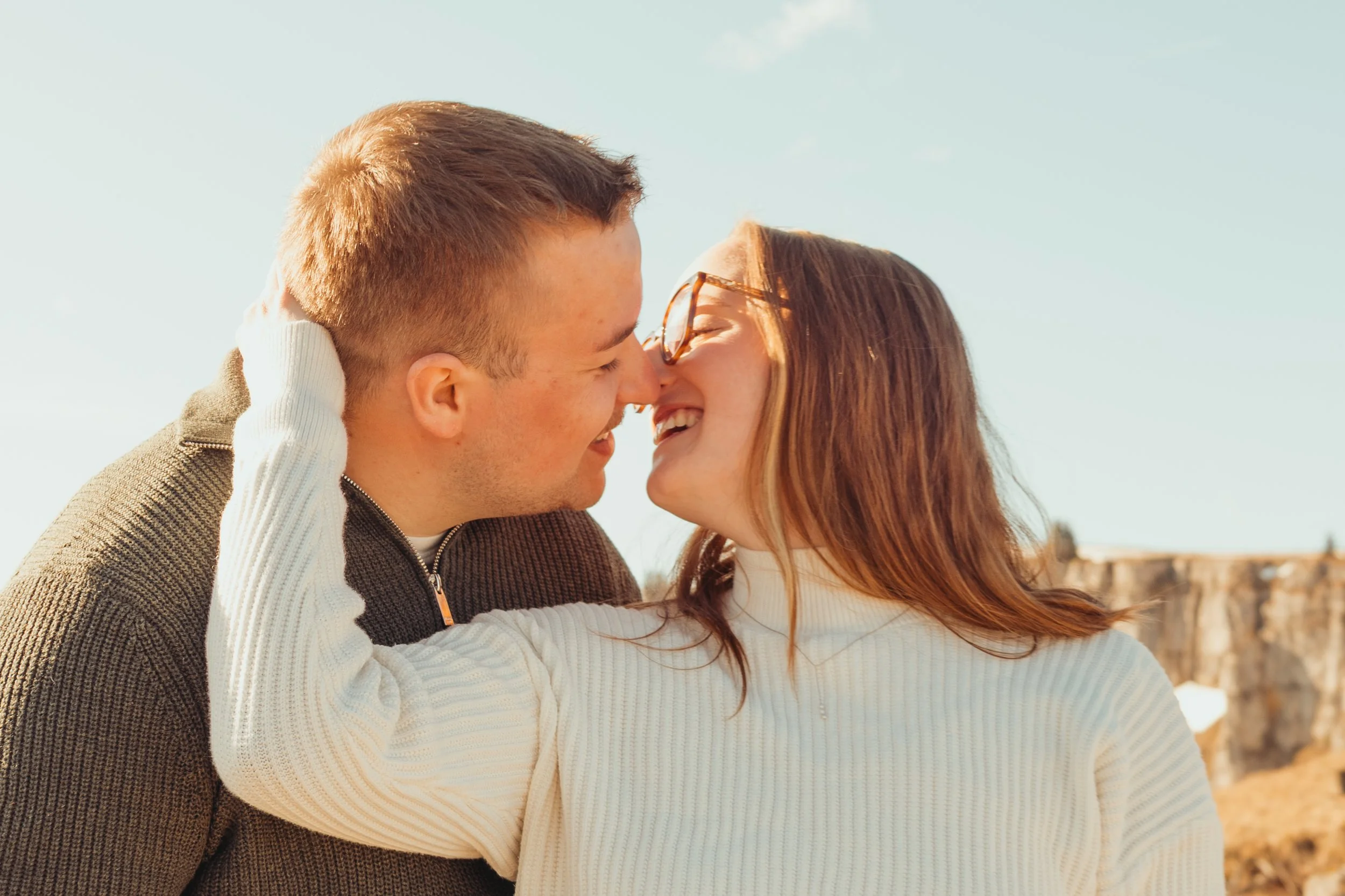 Un couple souriant s'embrassant près de la mer sous un ciel clair.