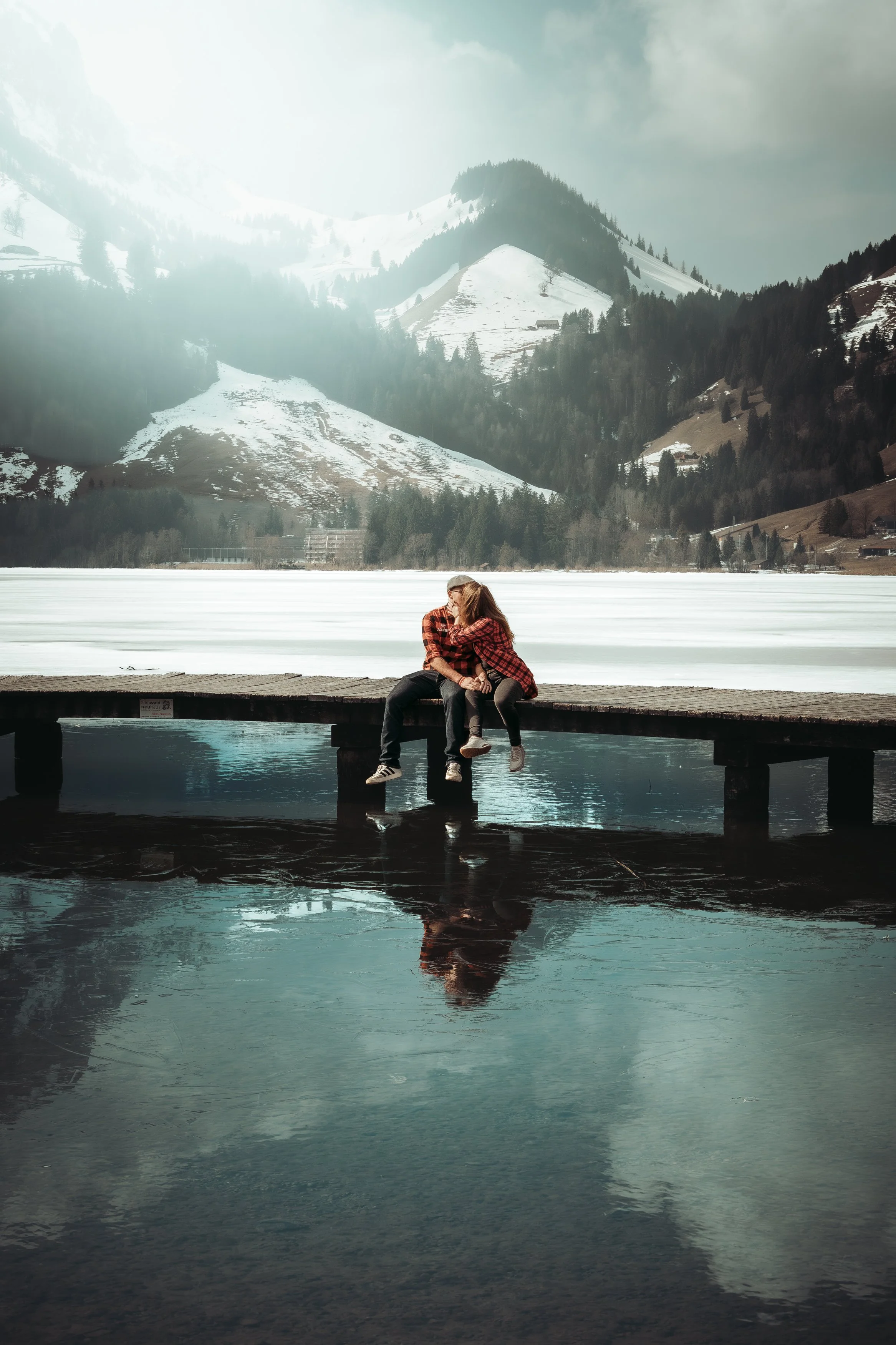 Deux enfants s'embrassent sur une jetée en bois au bord d'un lac gelé avec des montagnes enneigées en arrière-plan