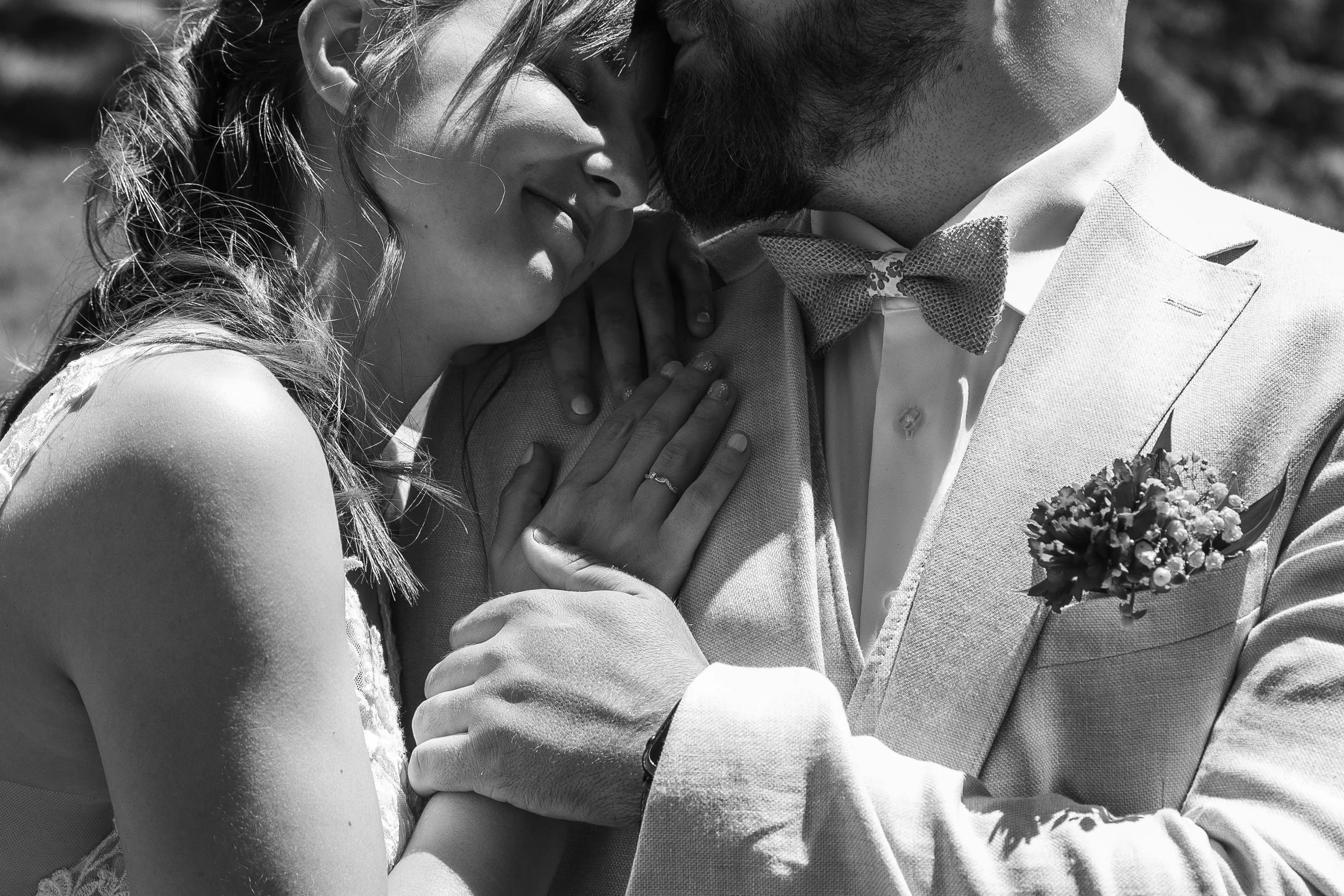 Un couple de mariés partage un moment intime, leur front et leur nez se touchant, avec une femme portant une robe de mariée et un homme en costume avec une fleur de boutonnière.
