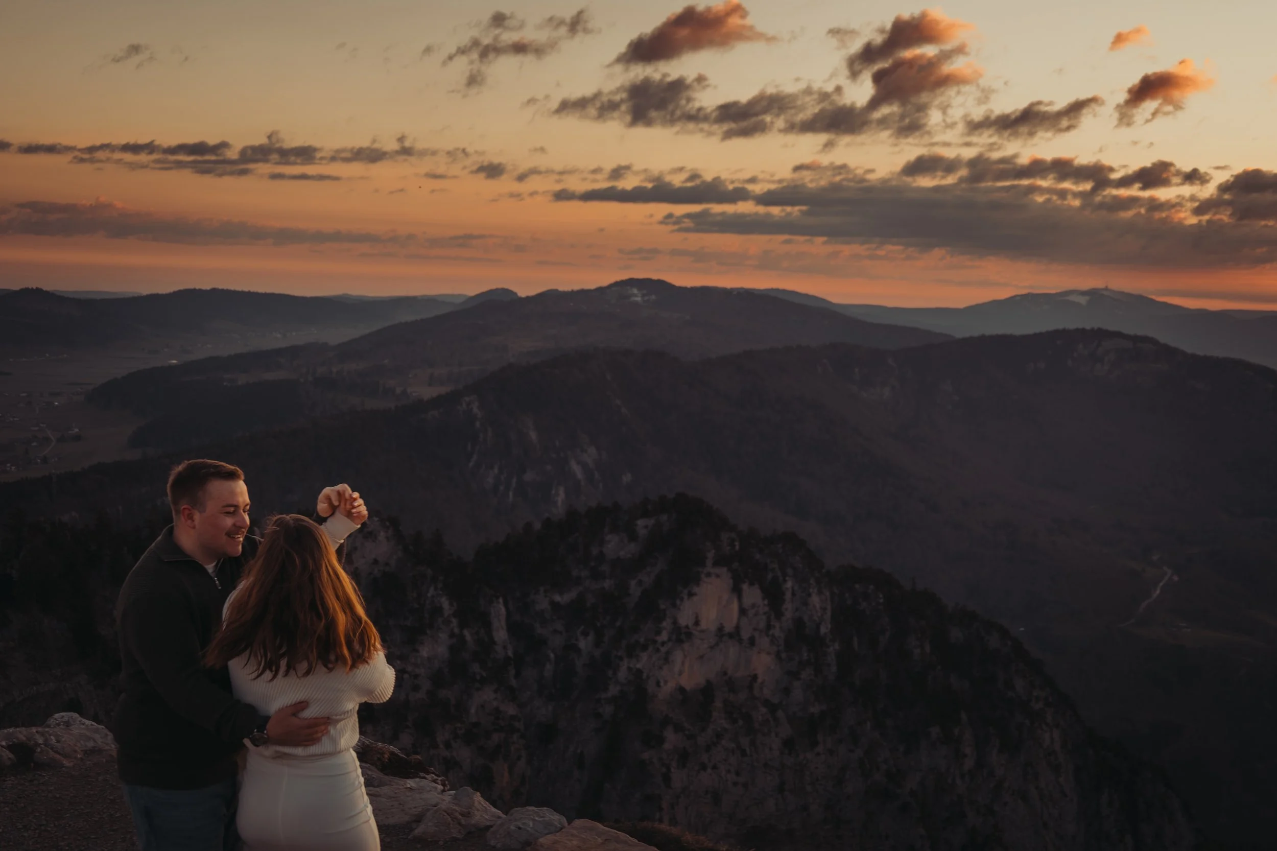 Un groupe de personnes célébrant lors d'un coucher de soleil à la montagne avec un ciel nuageux orange et sombre.