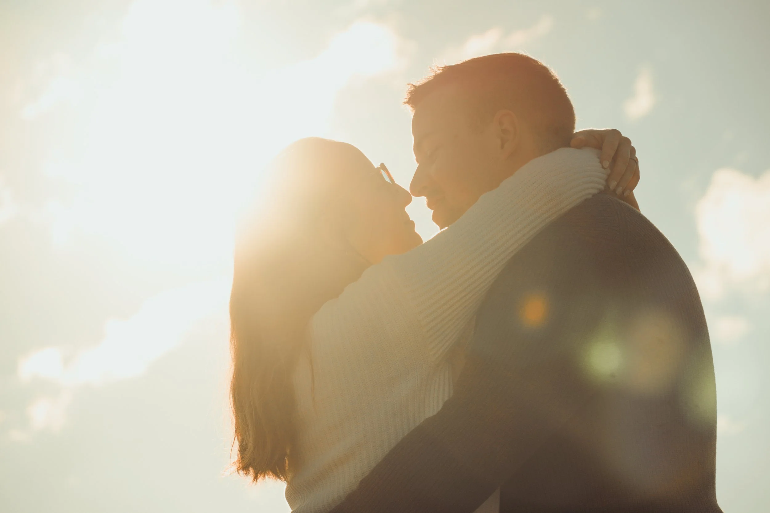 Un couple s'embrassant en plein air avec le soleil en arrière-plan.