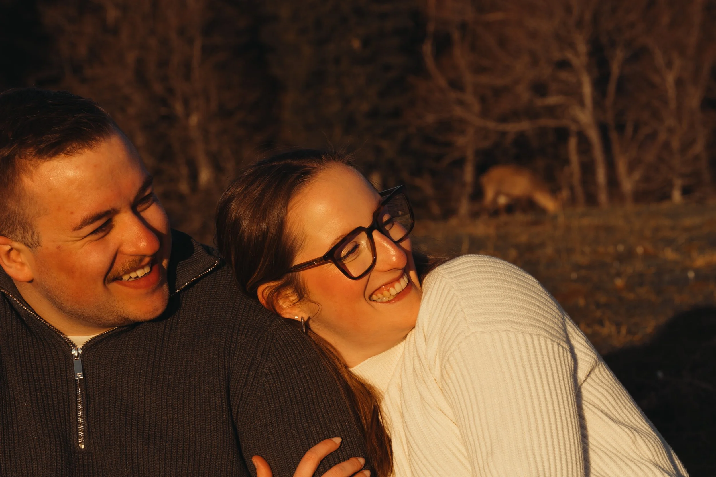 Deux personnes souriantes, un homme et une femme, prises en gros plan avec un arrière-plan de nature en soirée.