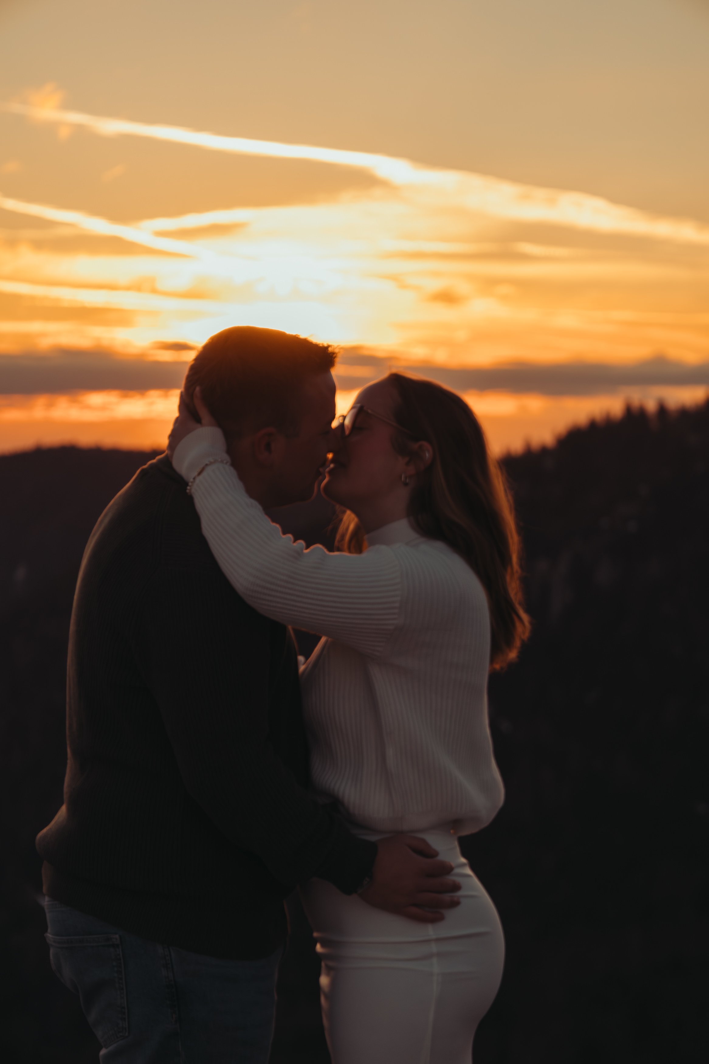 Un couple s'embrassant lors d'un coucher de soleil, avec un ciel orangé et nuageux en arrière-plan.