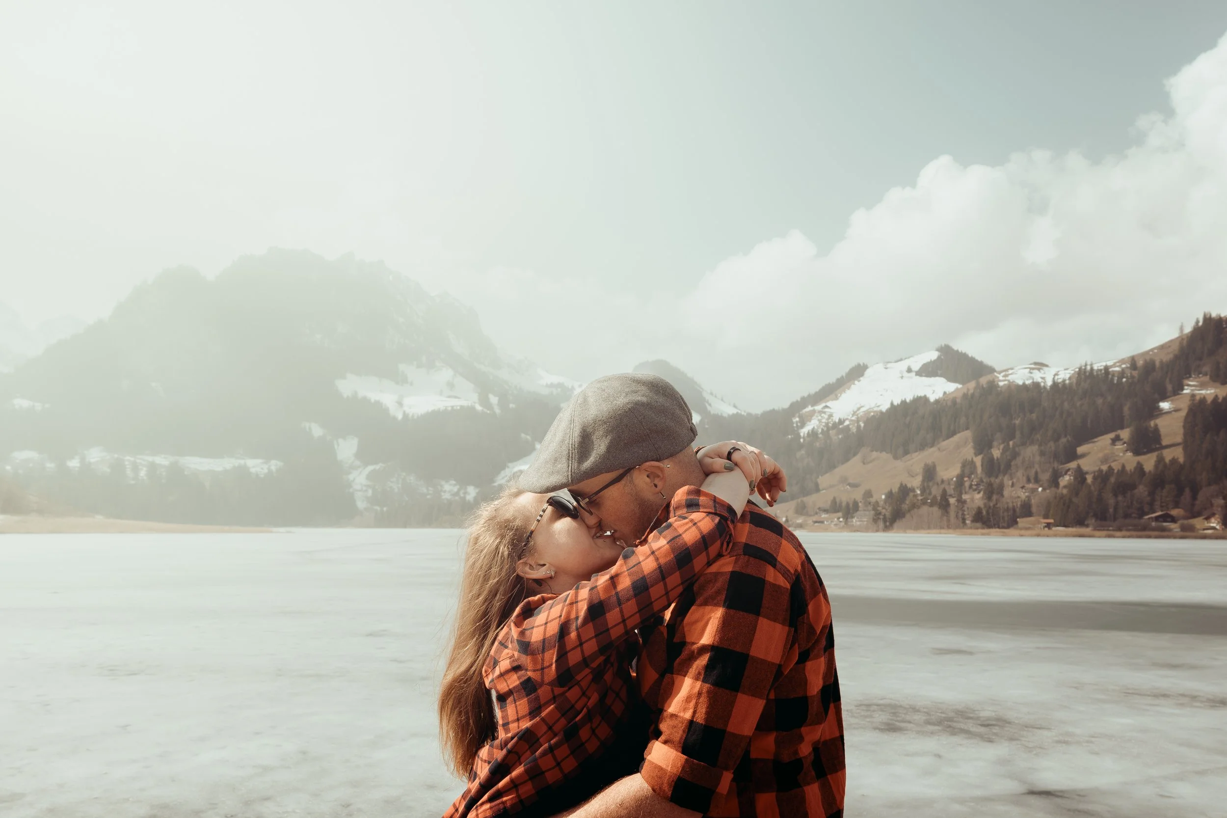 Un couple s'embrasse en pleine nature avec des montagnes enneigées en arrière-plan.