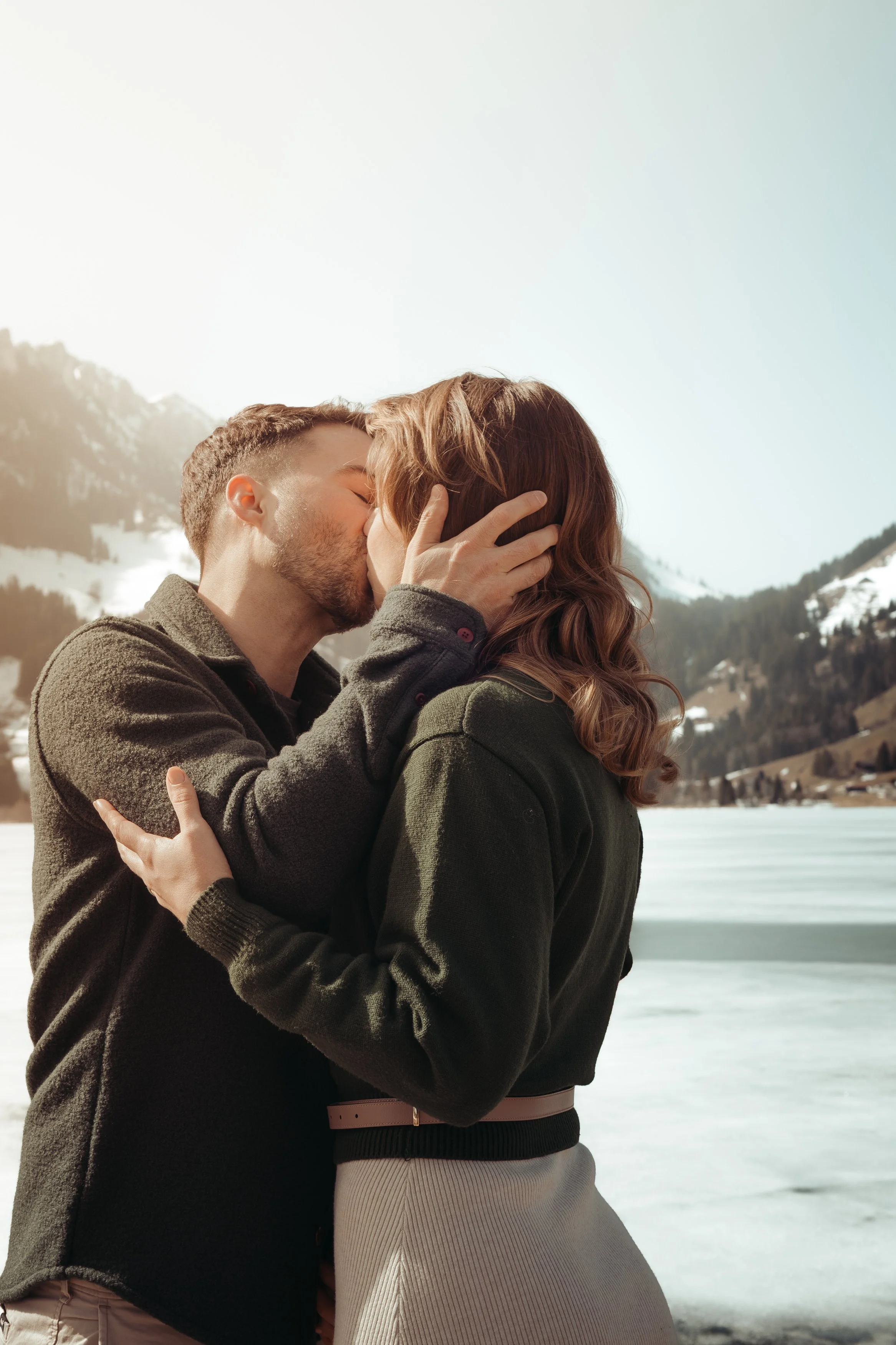 Un couple qui s'embrasse dans un paysage enneigé avec des montagnes en arrière-plan.