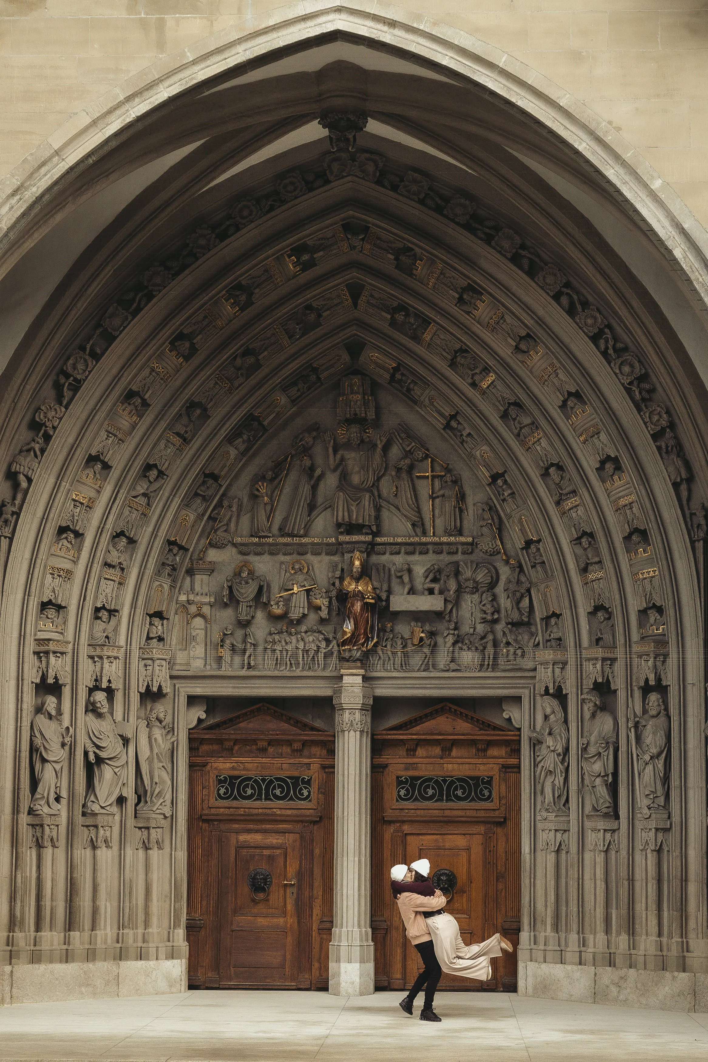 Un couple de femmes lesbiennes s'embrassent devant la grande porte en bois de la cathédrale de Fribourg.