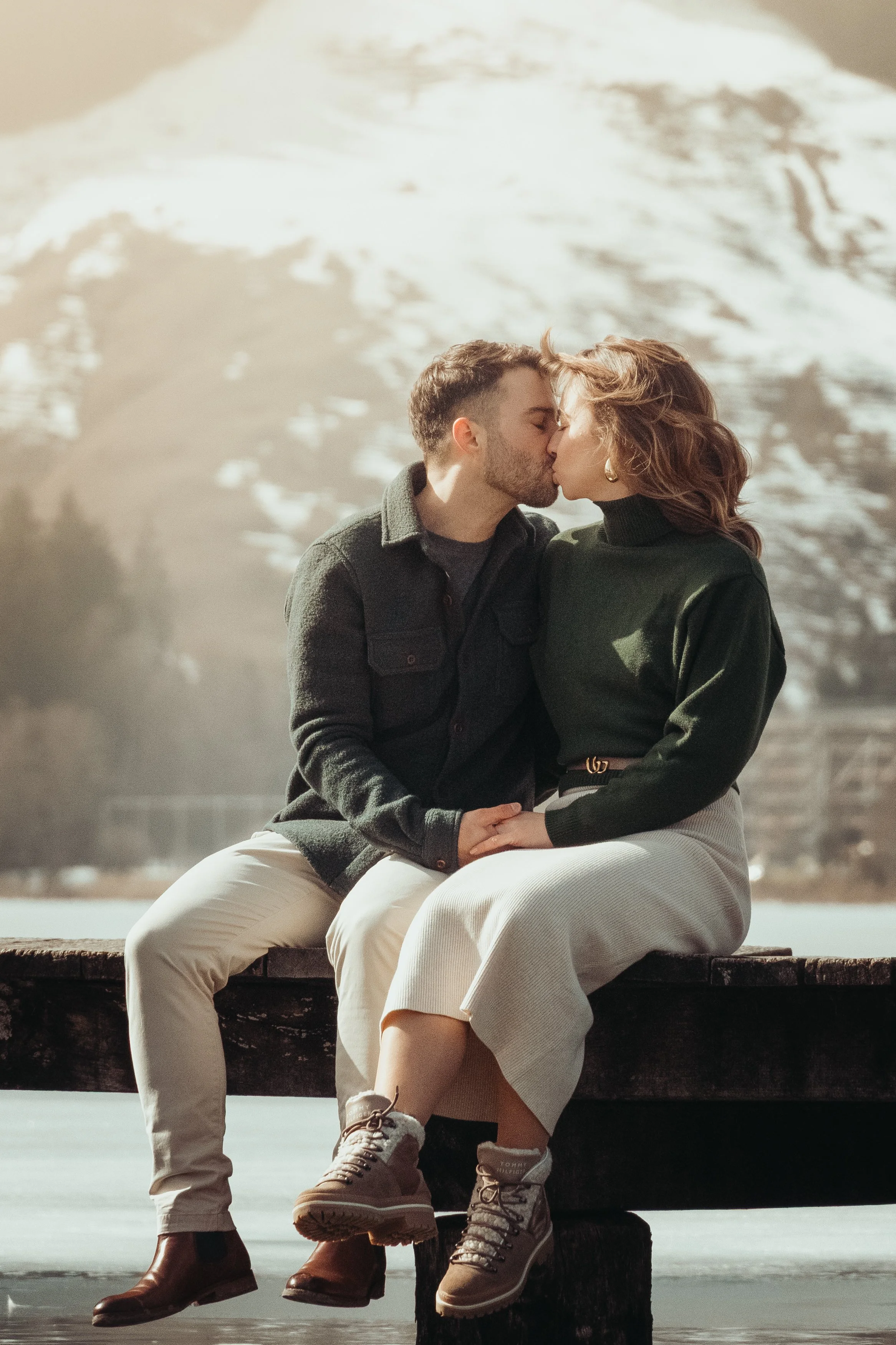 Un couple s'embrasse en s'asseyant sur un banc près de l'eau, avec un glacier en arrière-plan.