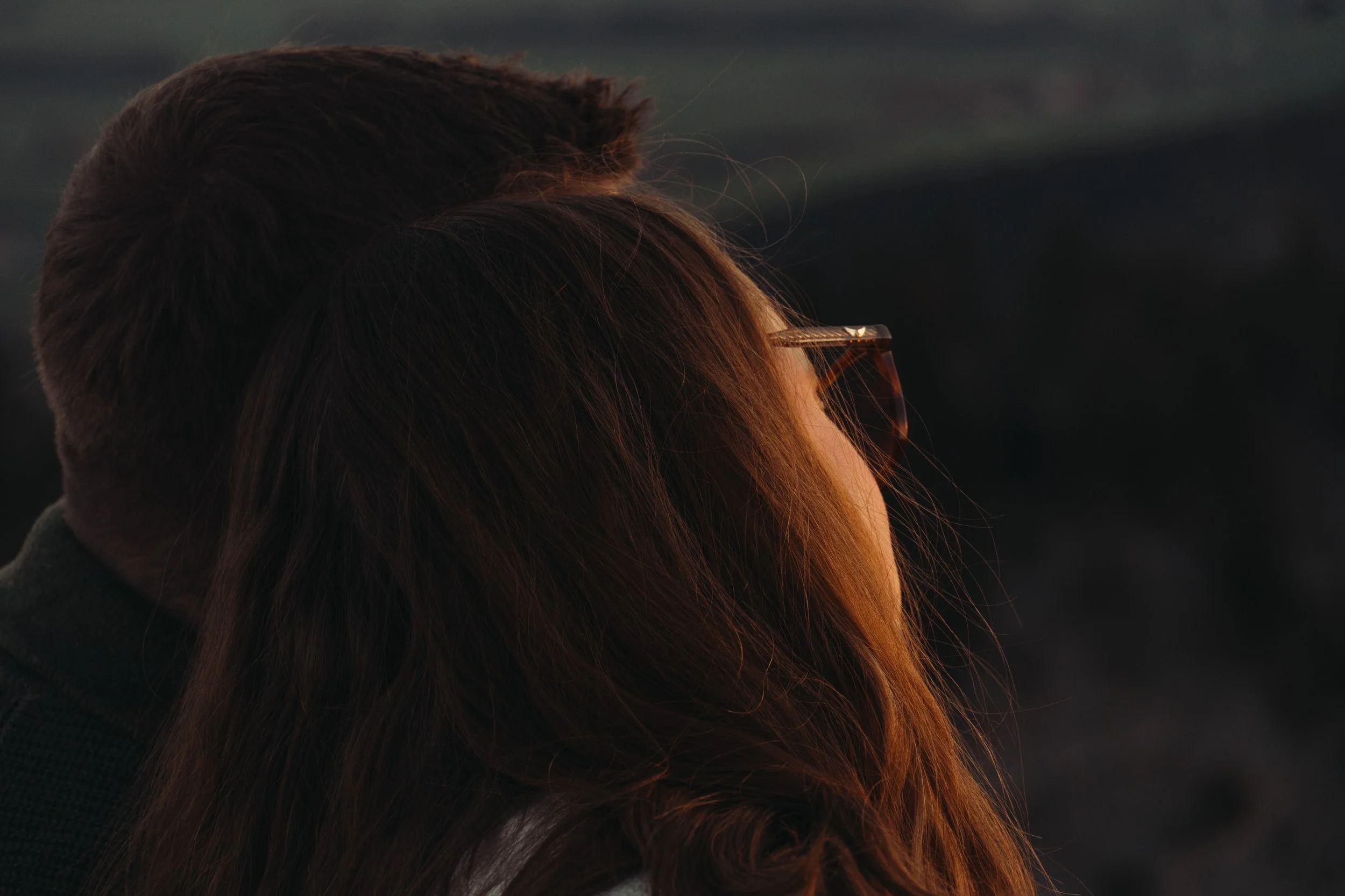 Femme avec des cheveux longs et bruns portant des lunettes de soleil, vue de profil dans un éclairage tamisé.